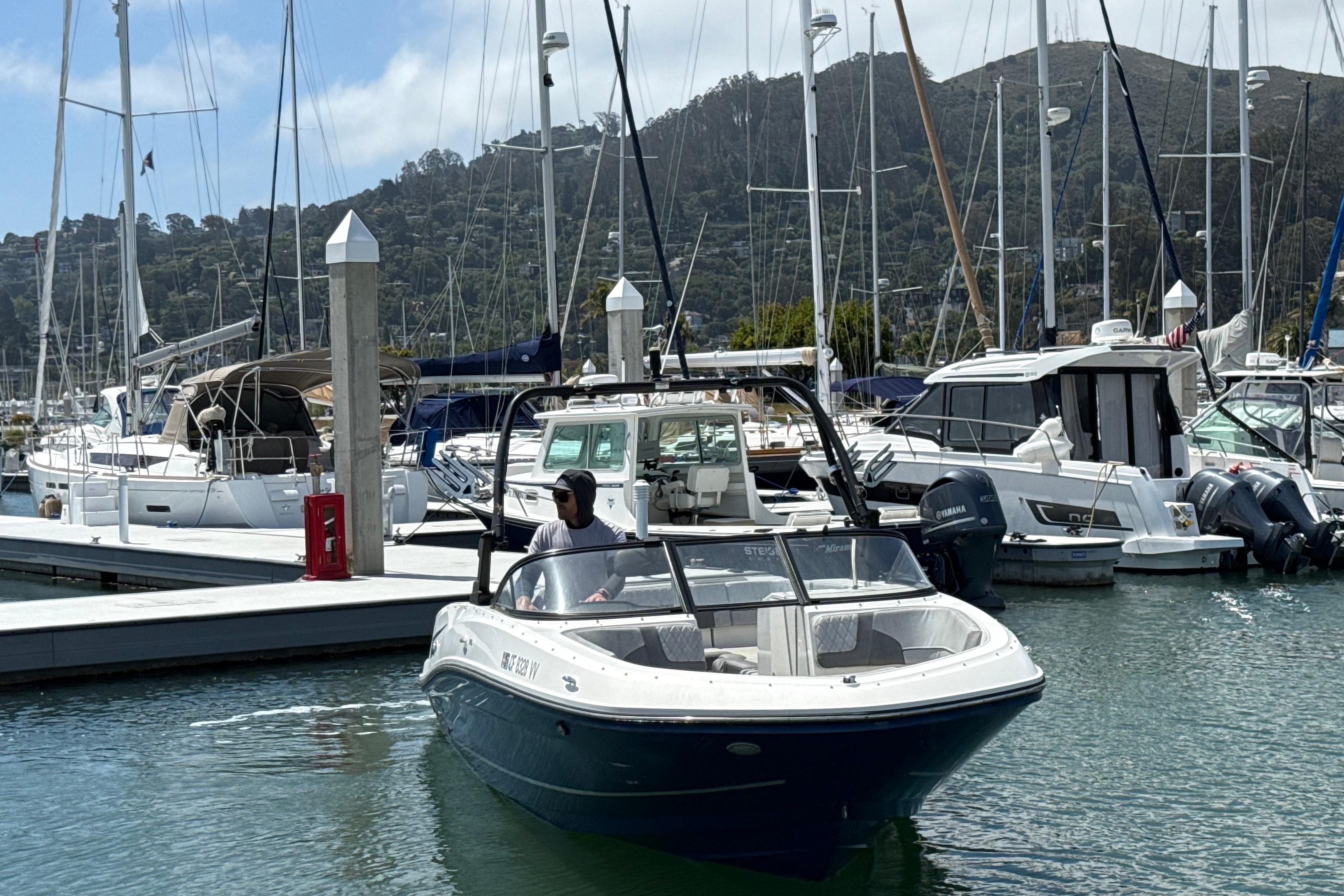 2021 Bayliner VR5 Bowrider I/O navigating marina, surrounded by docked boats and scenic hills.