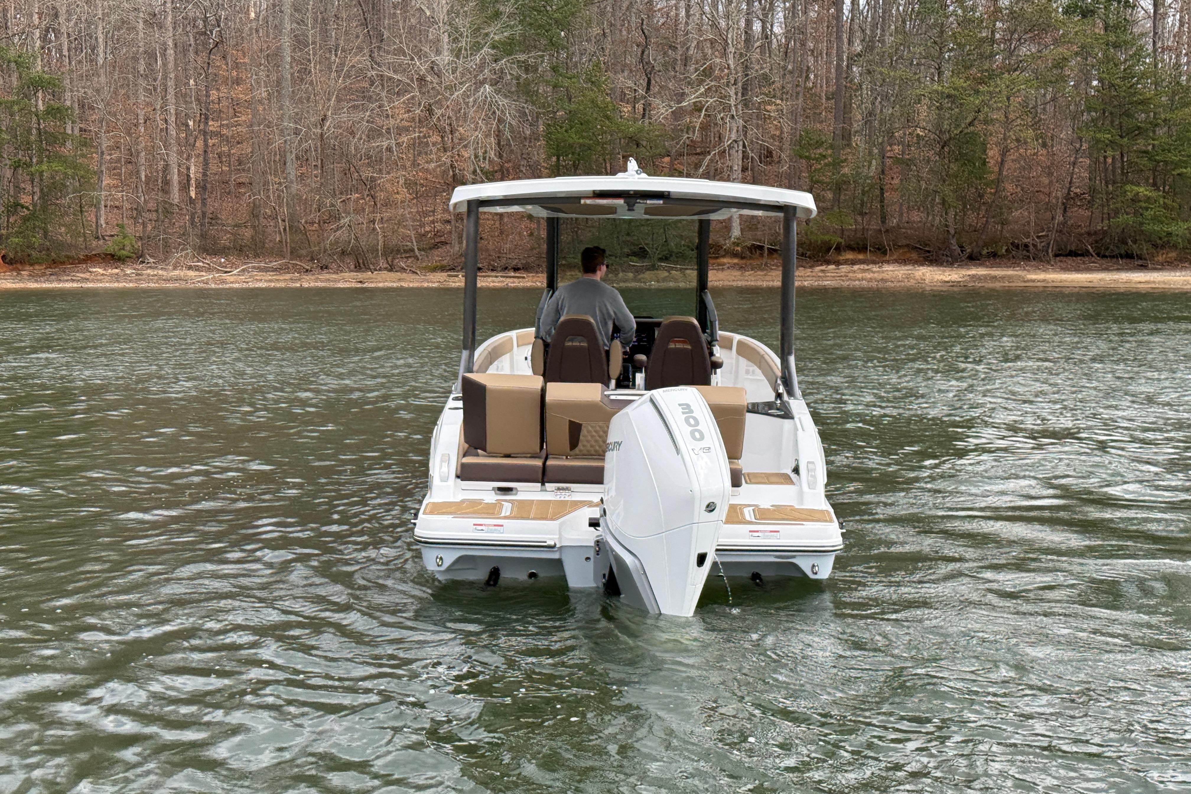 2026 Monterey Elite 25 OB boat cruising on a calm lake with wooded shoreline.