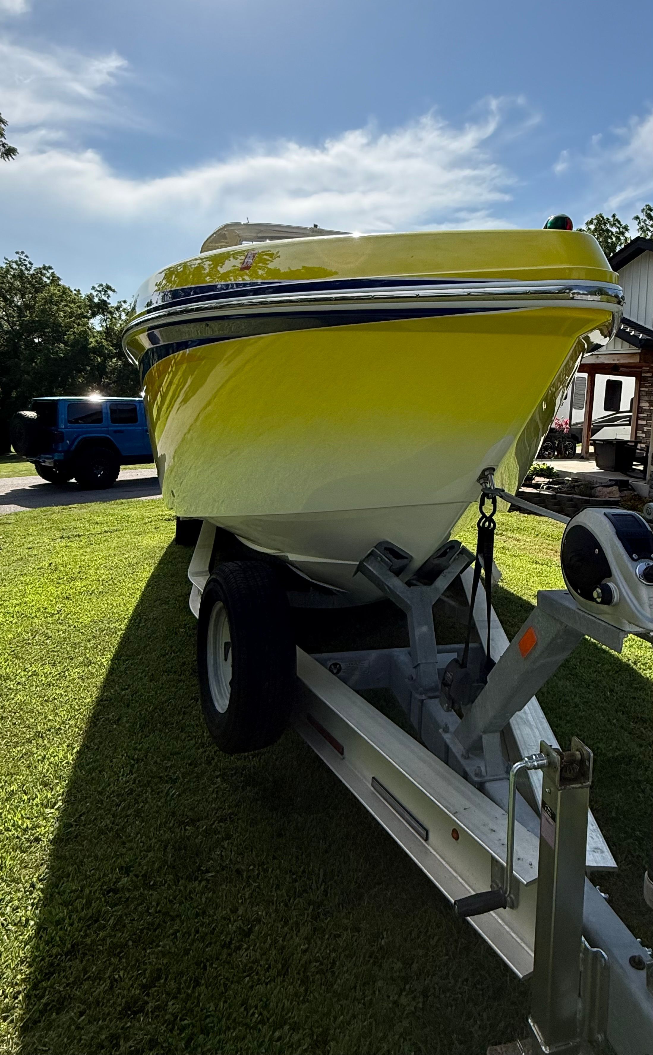 A yellow boat on a trailer on grass, with a blue sky in the background.