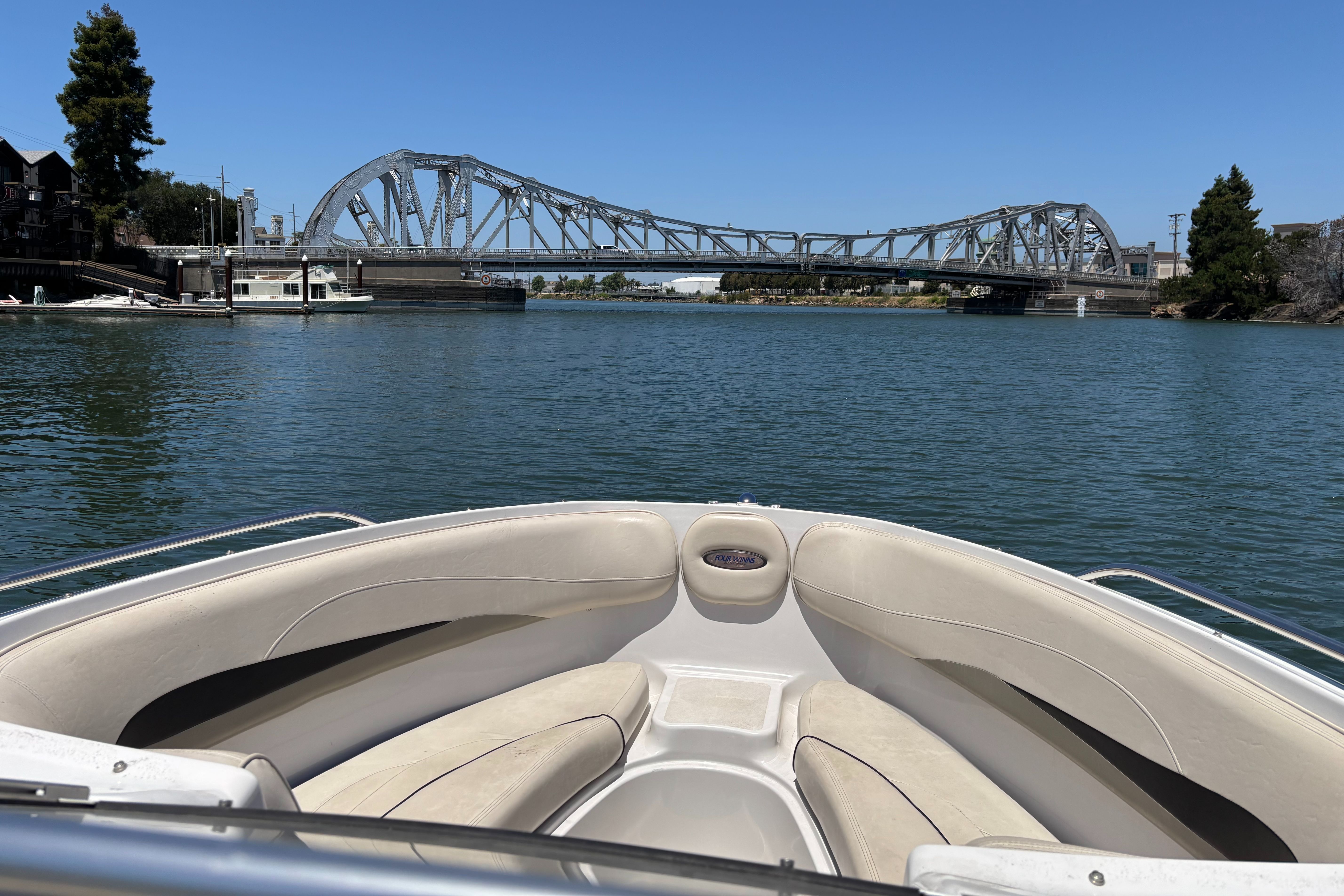 The boat is a 2000 Four Winns 220 Horizon. It cruises on a calm river under a bridge.