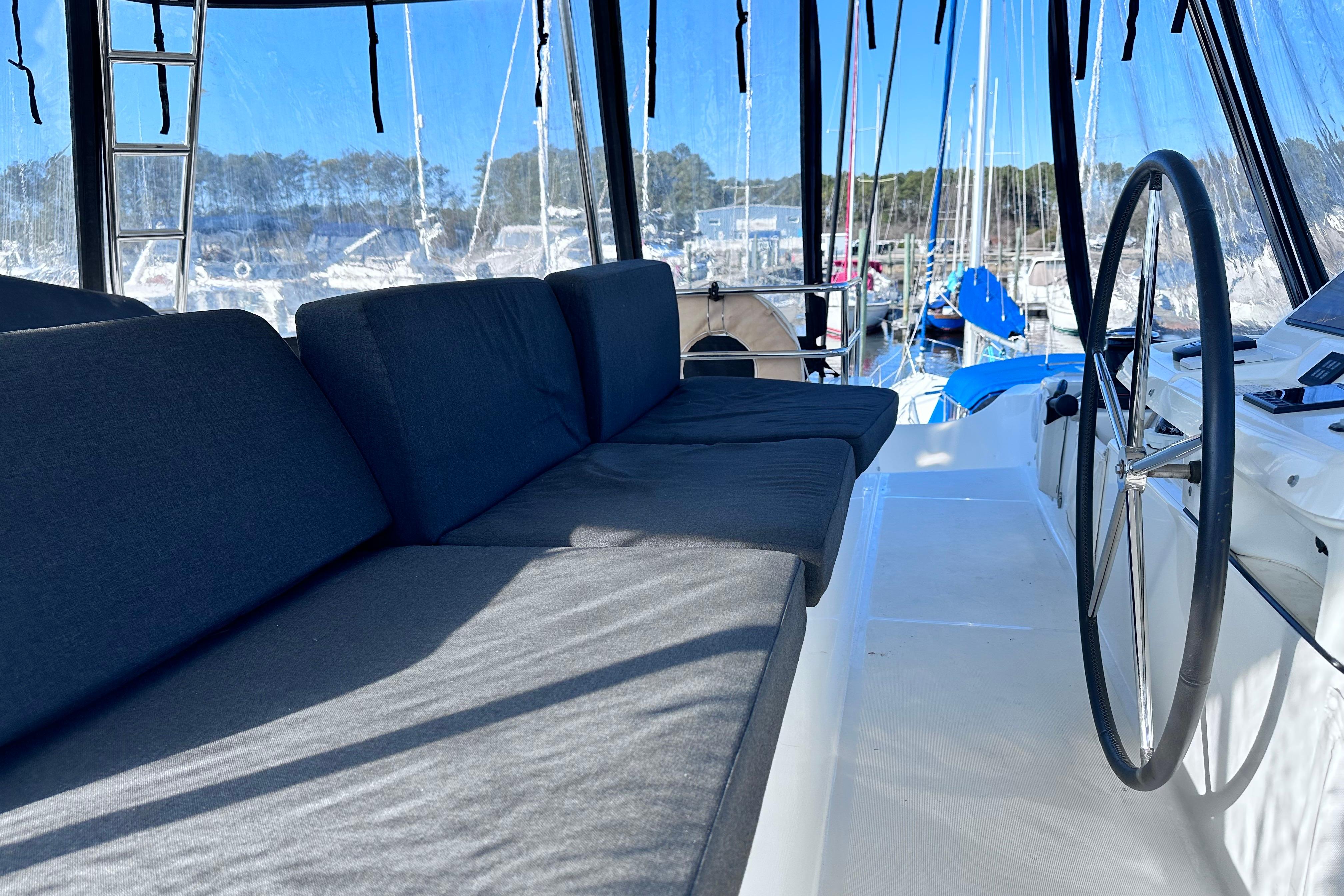2023 Lagoon 50 yacht cockpit with cushioned seating and steering wheel, docked at marina.