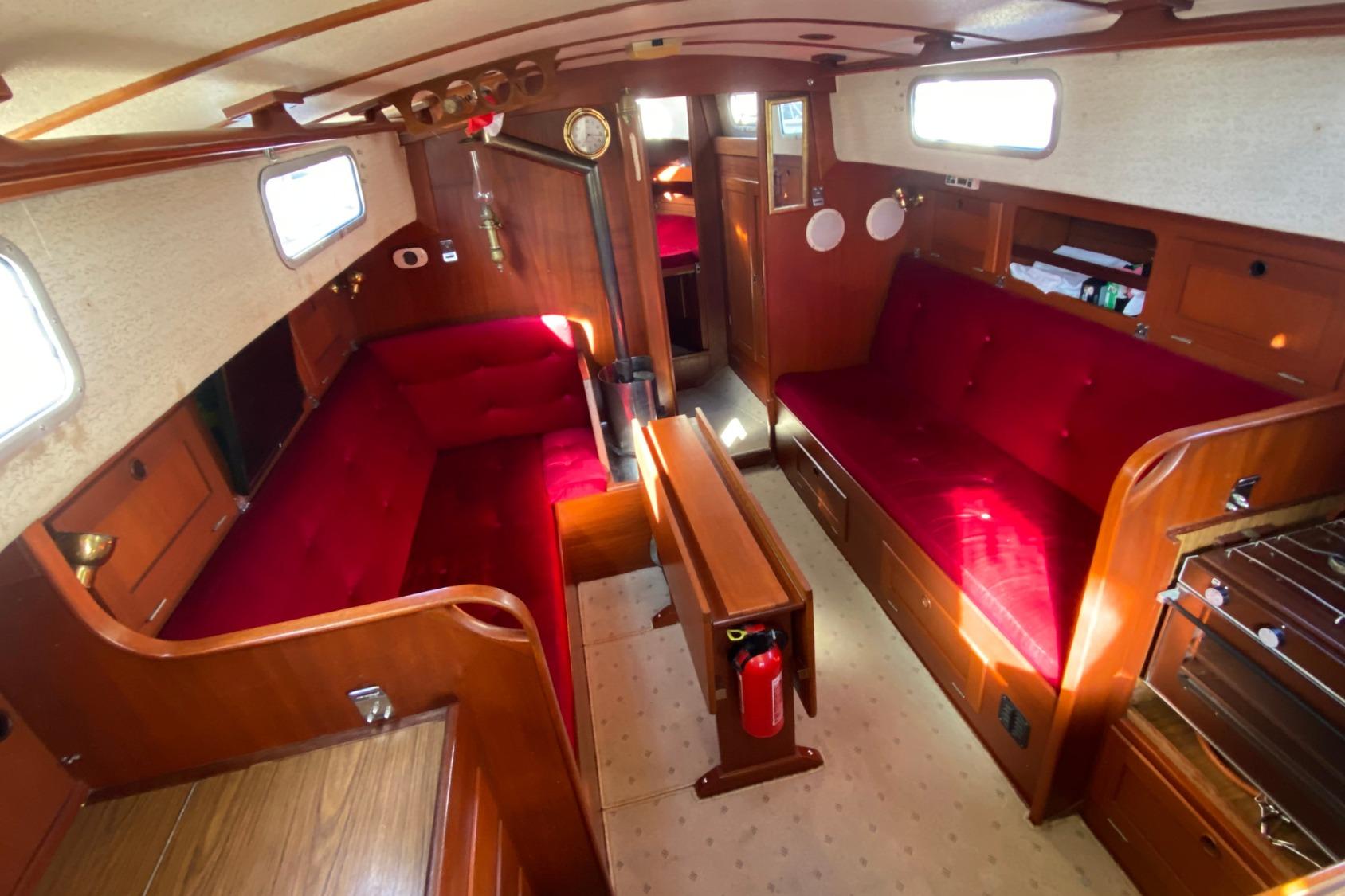 Interior of 1983 Hallberg-Rassy 94 Kutter sailboat with red upholstery and wooden finishes.