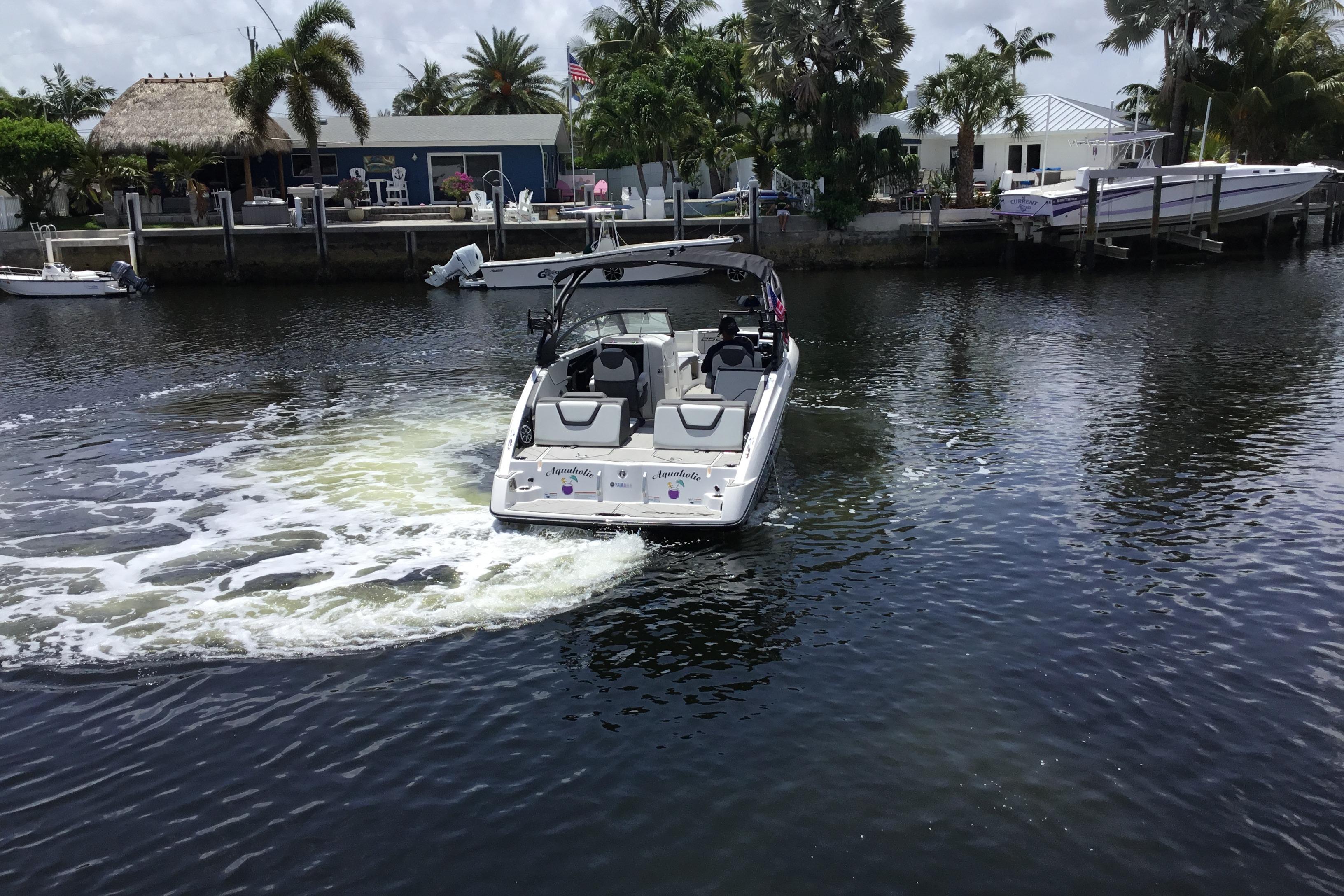 2023 Yamaha Boats 252XE cruising on a scenic waterway near waterfront homes.