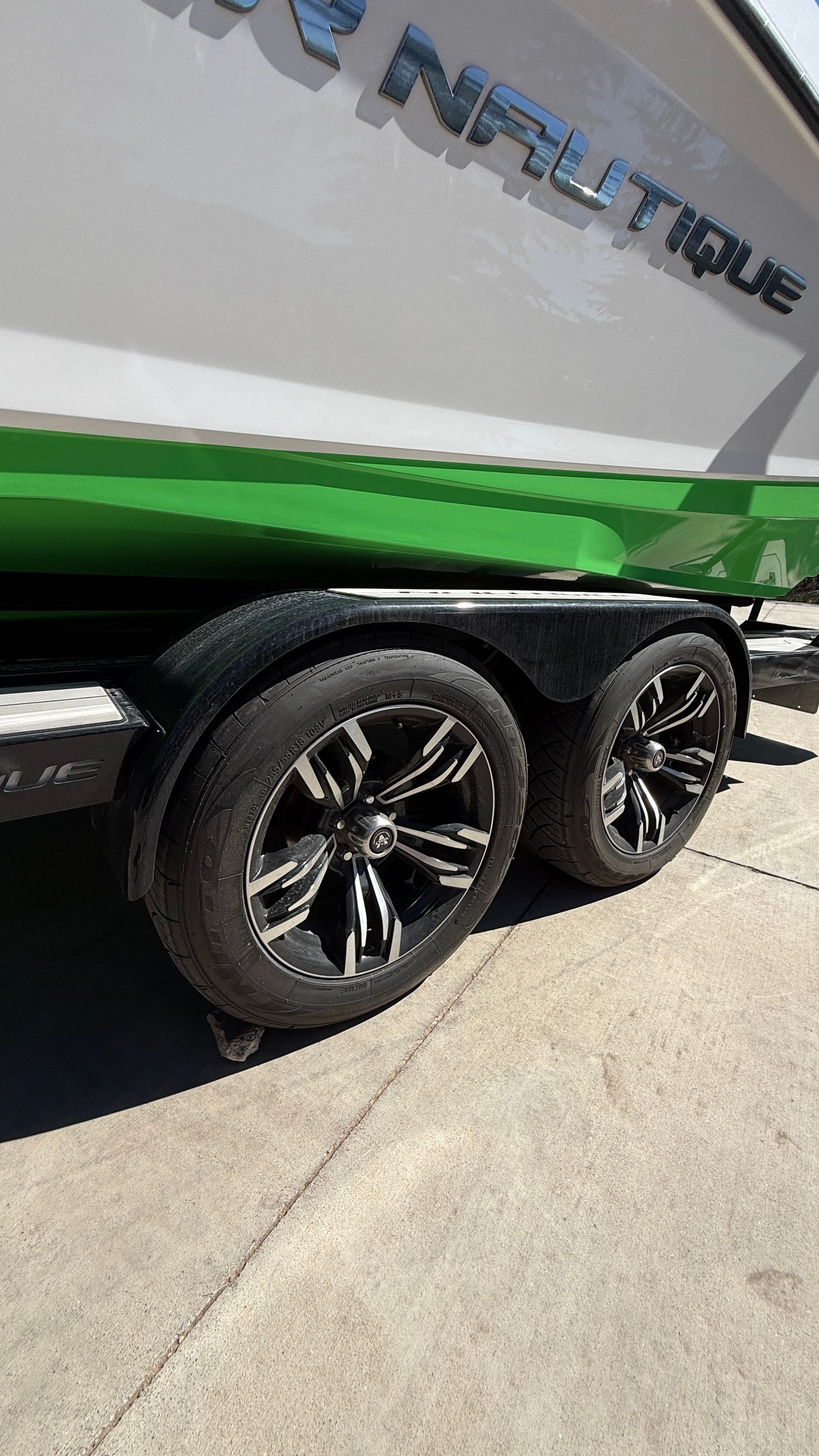 Close-up of a boat trailer with two stylish wheels carrying a green and white boat.