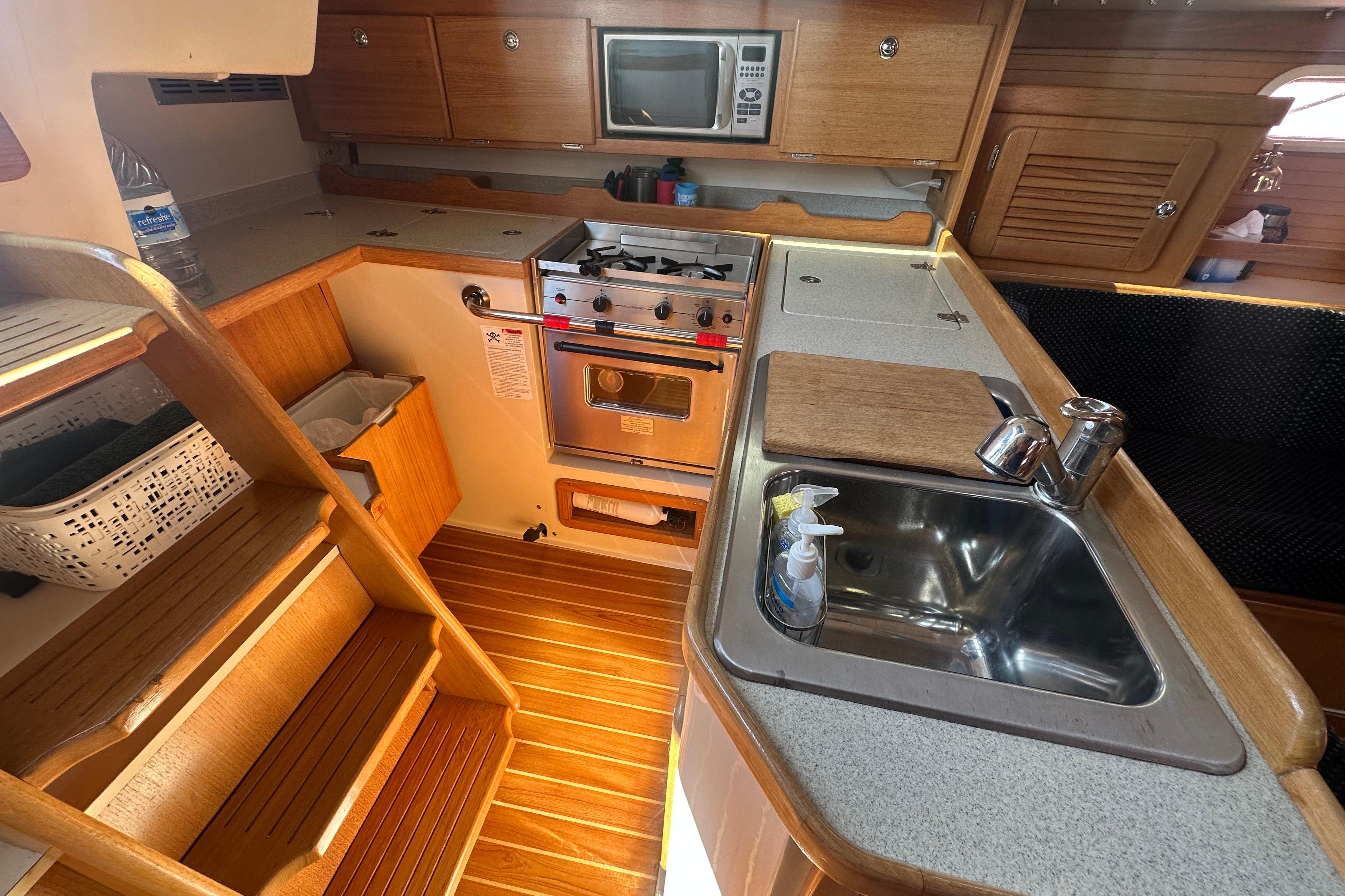 2005 Catalina 36 MkII yacht kitchen with wooden cabinetry, stove, sink, and microwave.