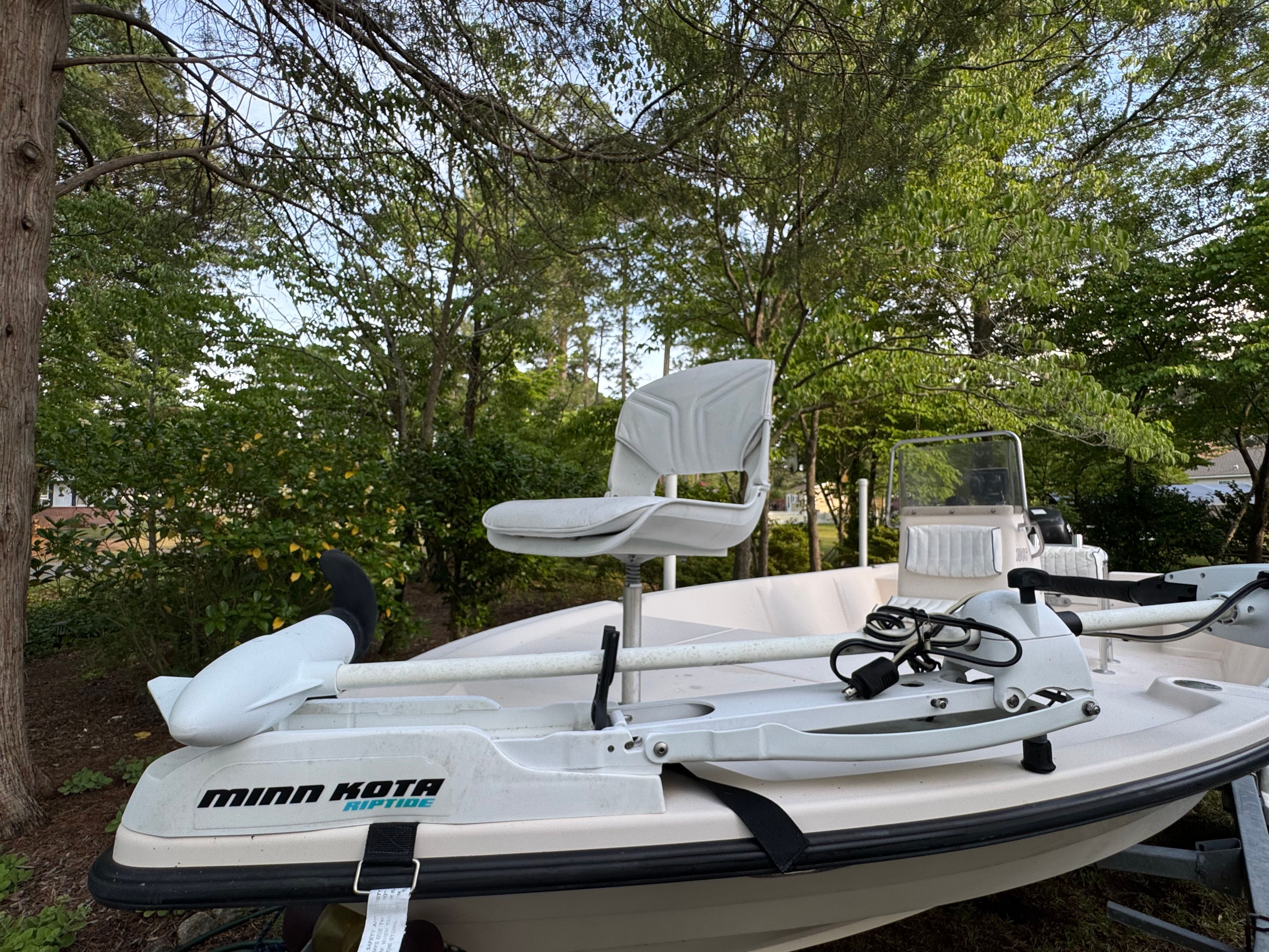 A white boat with a Minn Kota trolling motor and elevated seat, surrounded by trees.