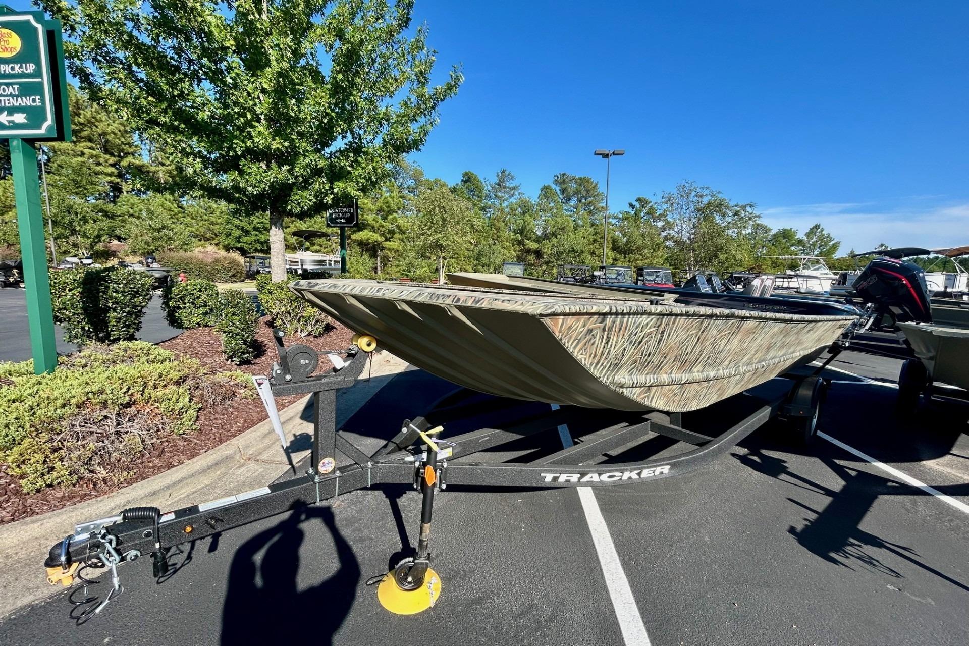 2026 Tracker Grizzly 2072 Utility boat on trailer in parking lot, surrounded by trees.