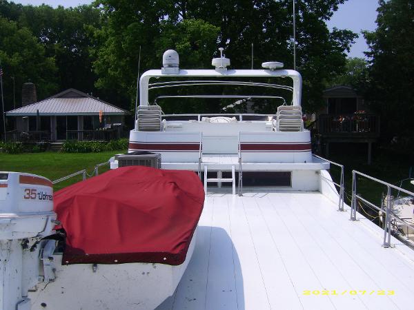 1980 Pluckebaum Baymaster boat with red cover, docked near lush greenery and houses.