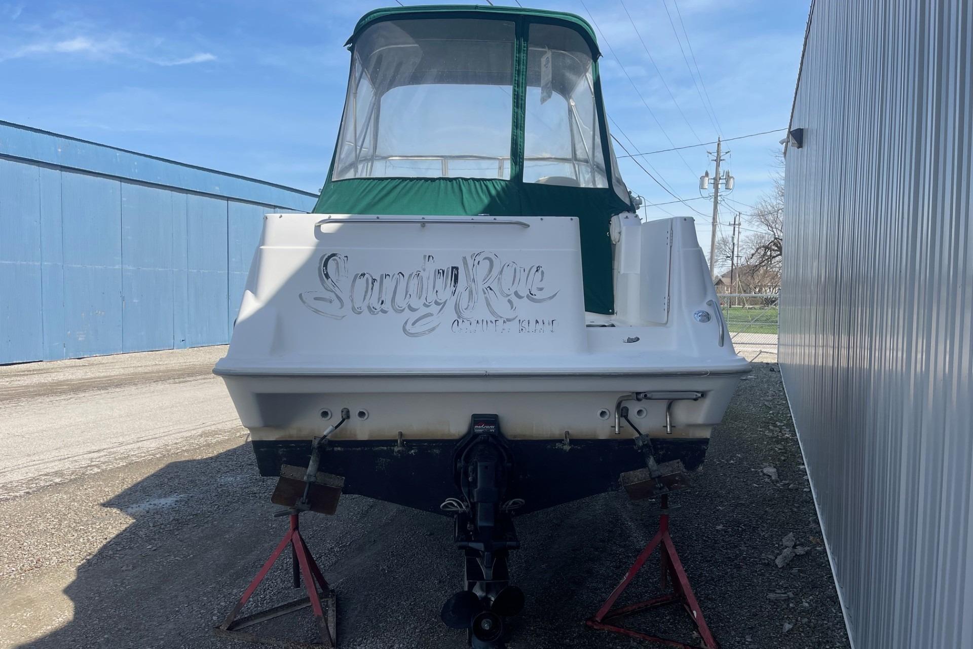 1997 Bayliner 2655 Ciera boat with green canopy, parked on stands near a building.