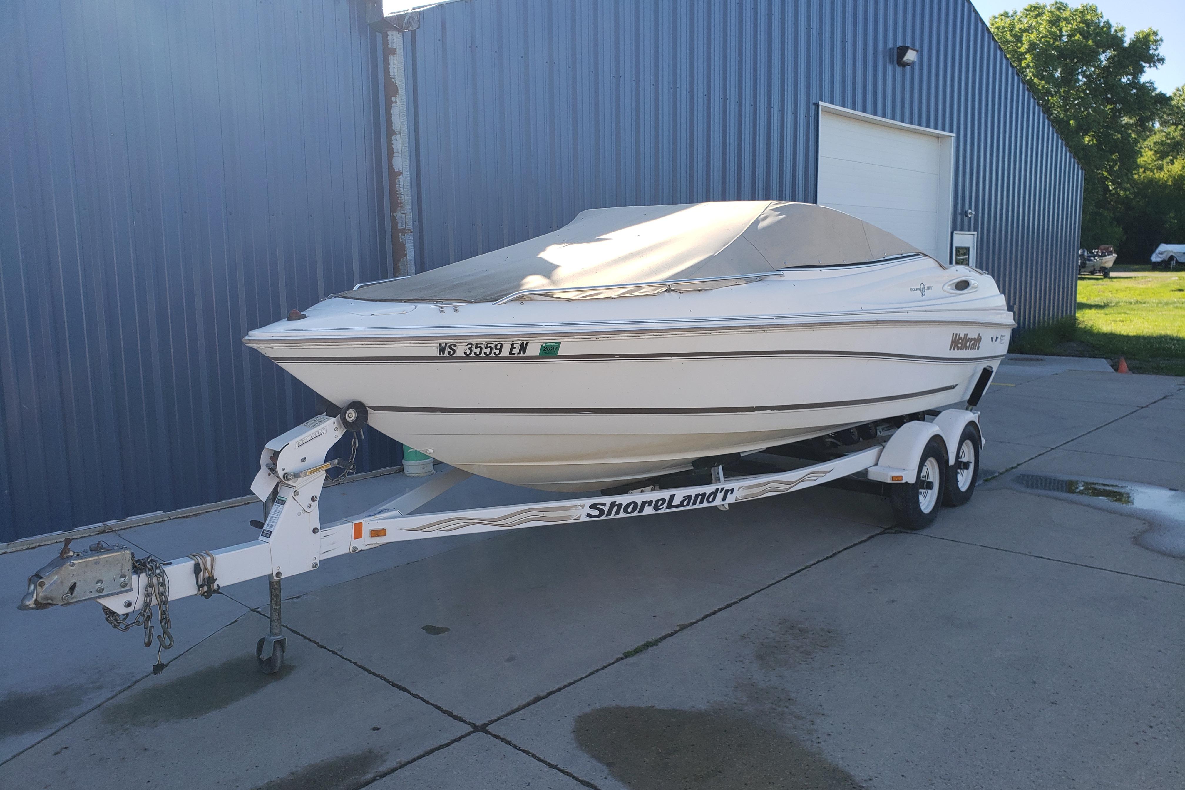 1998 Wellcraft Eclipse 2000 SS boat on ShoreLand'r trailer, parked by blue building.