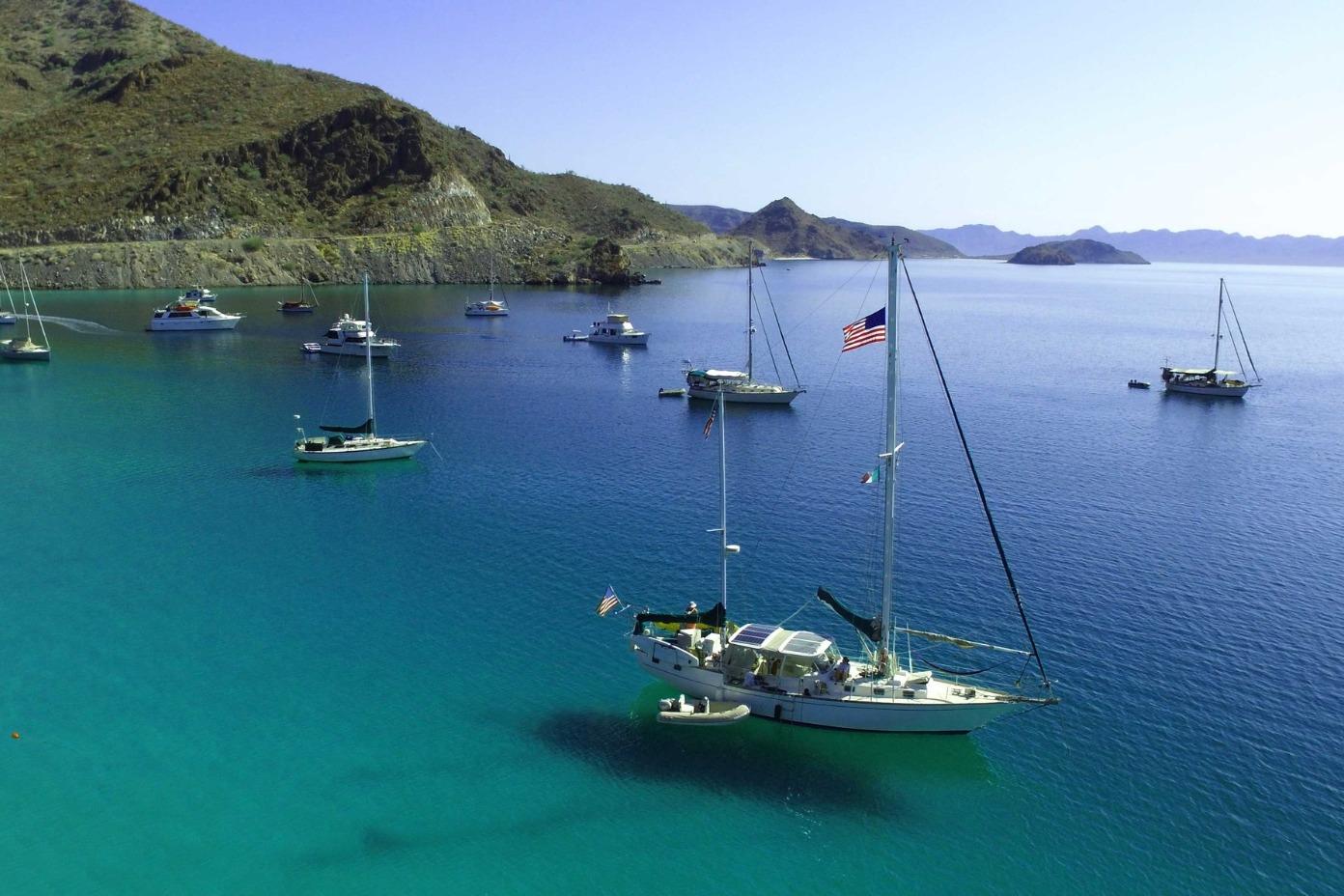 Sailboats anchored in a serene bay, featuring a 1978 Herreshoff 50 under clear blue skies.