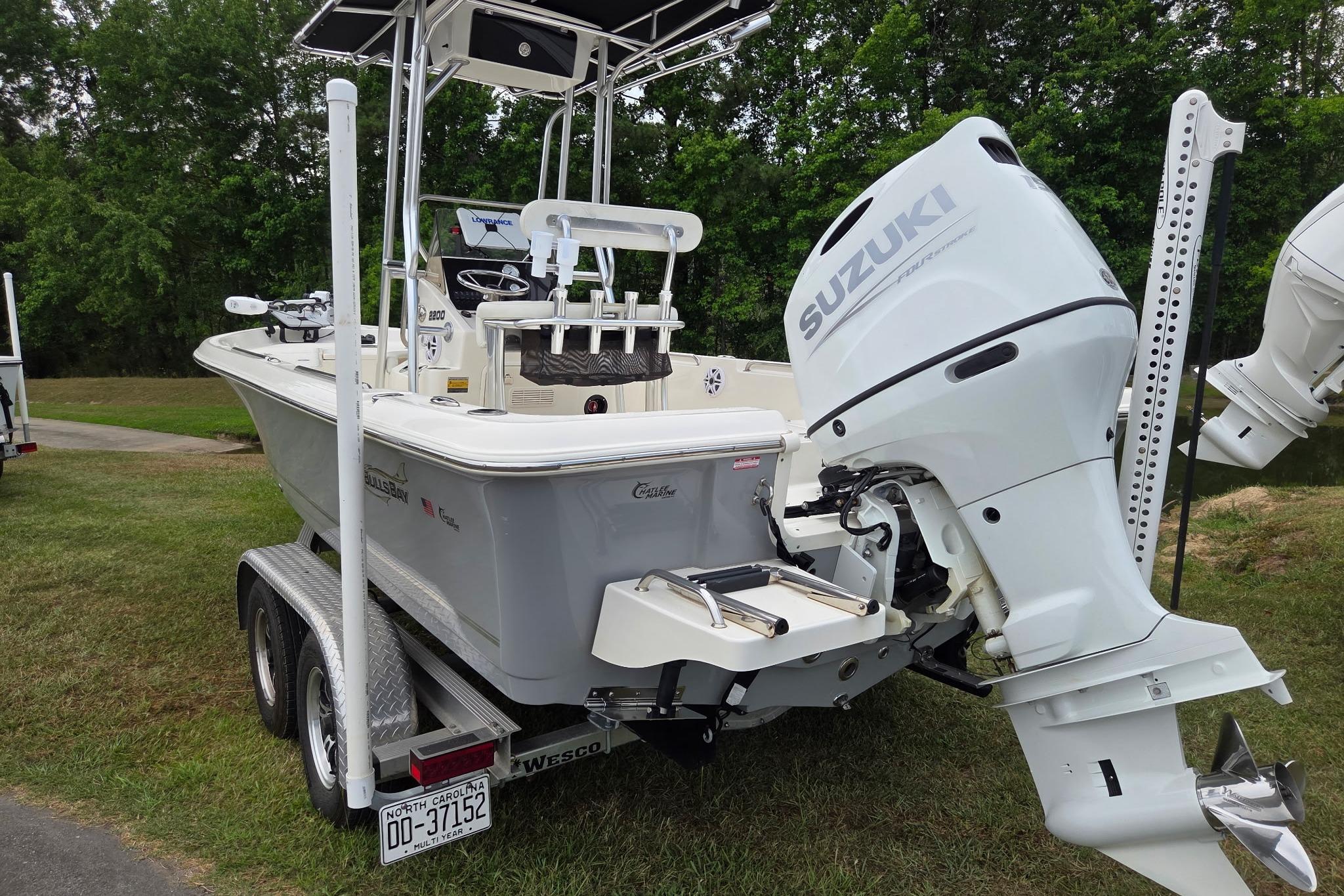 2023 Bulls Bay 2200 boat with Suzuki outboard motor on trailer, parked on grass.