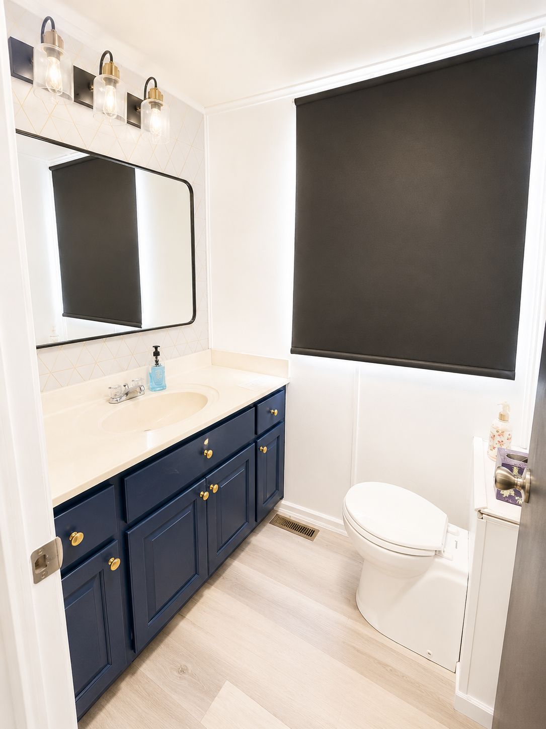 A modern bathroom with blue cabinets, a large mirror, and a toilet.