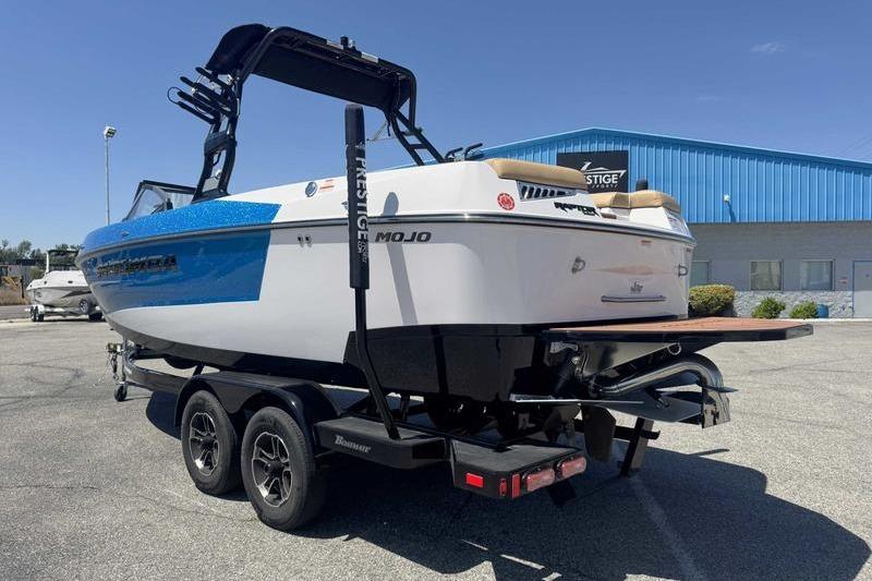 2023 Moomba Mojo Pro boat on trailer, parked outdoors near blue building.