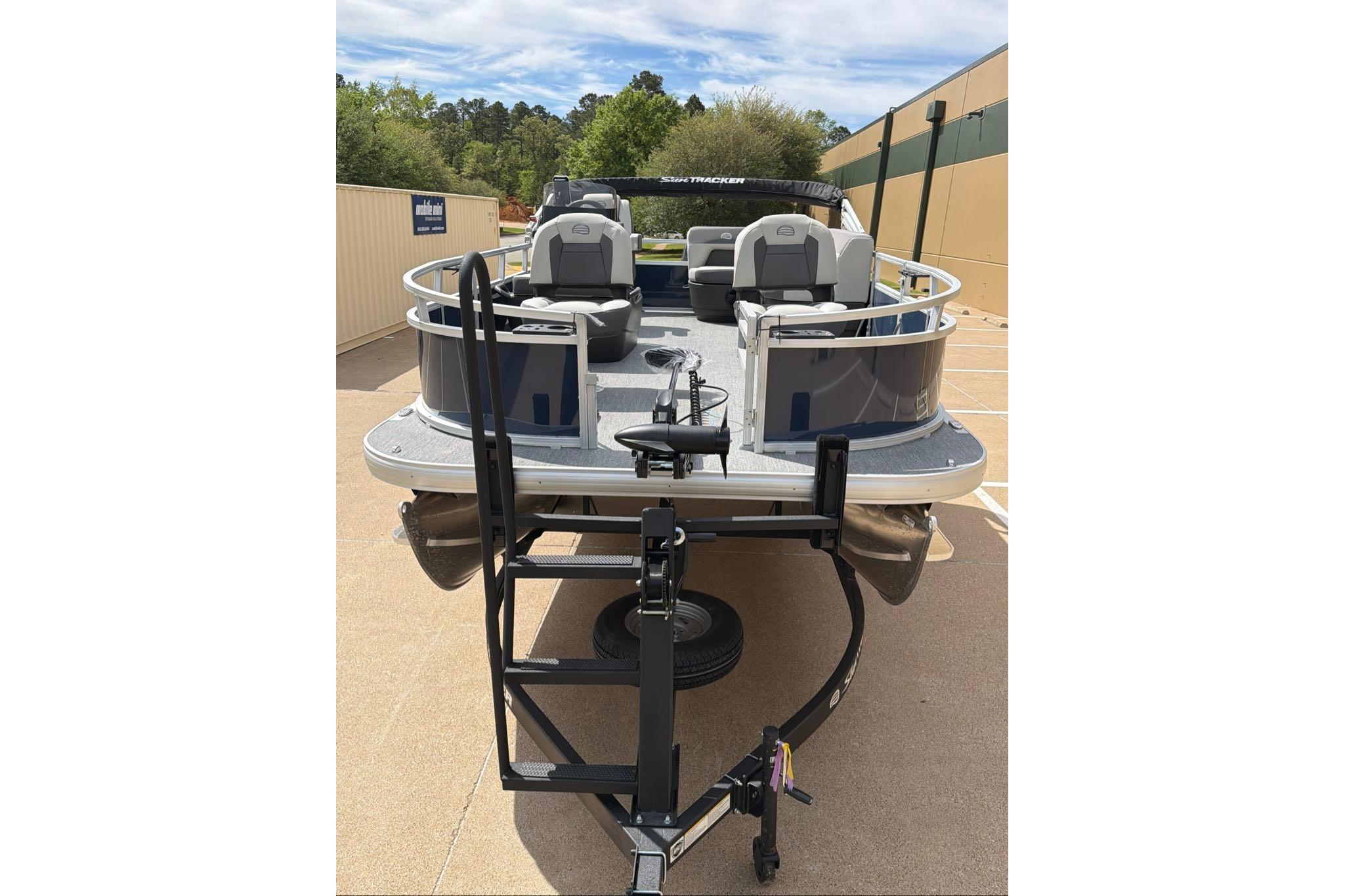 2026 Sun Tracker Bass Buggy 16 XL Select pontoon boat on trailer in parking lot.