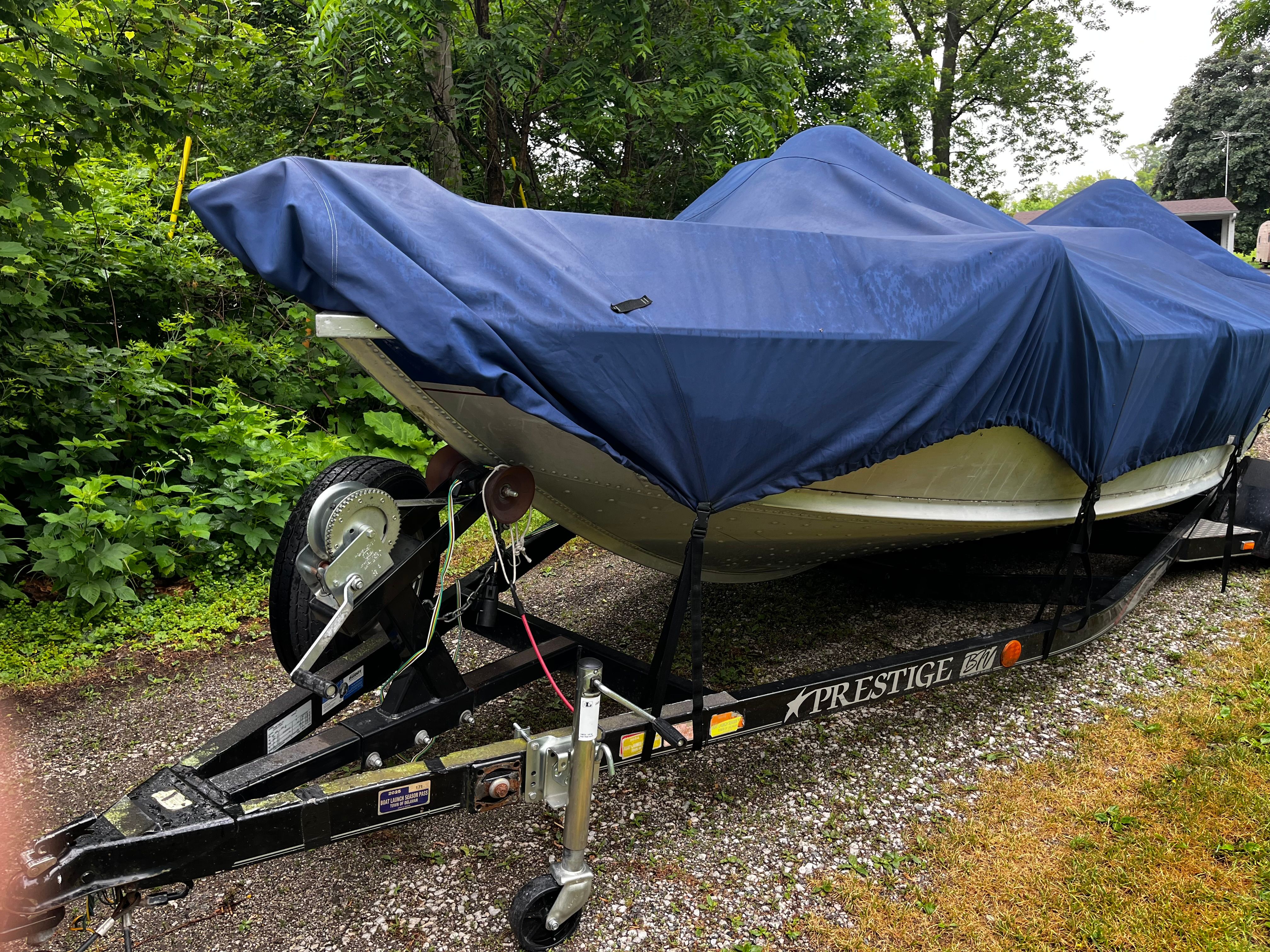 A 2005 Alumacraft Navigator 175CS boat on a trailer, covered with a blue tarp.