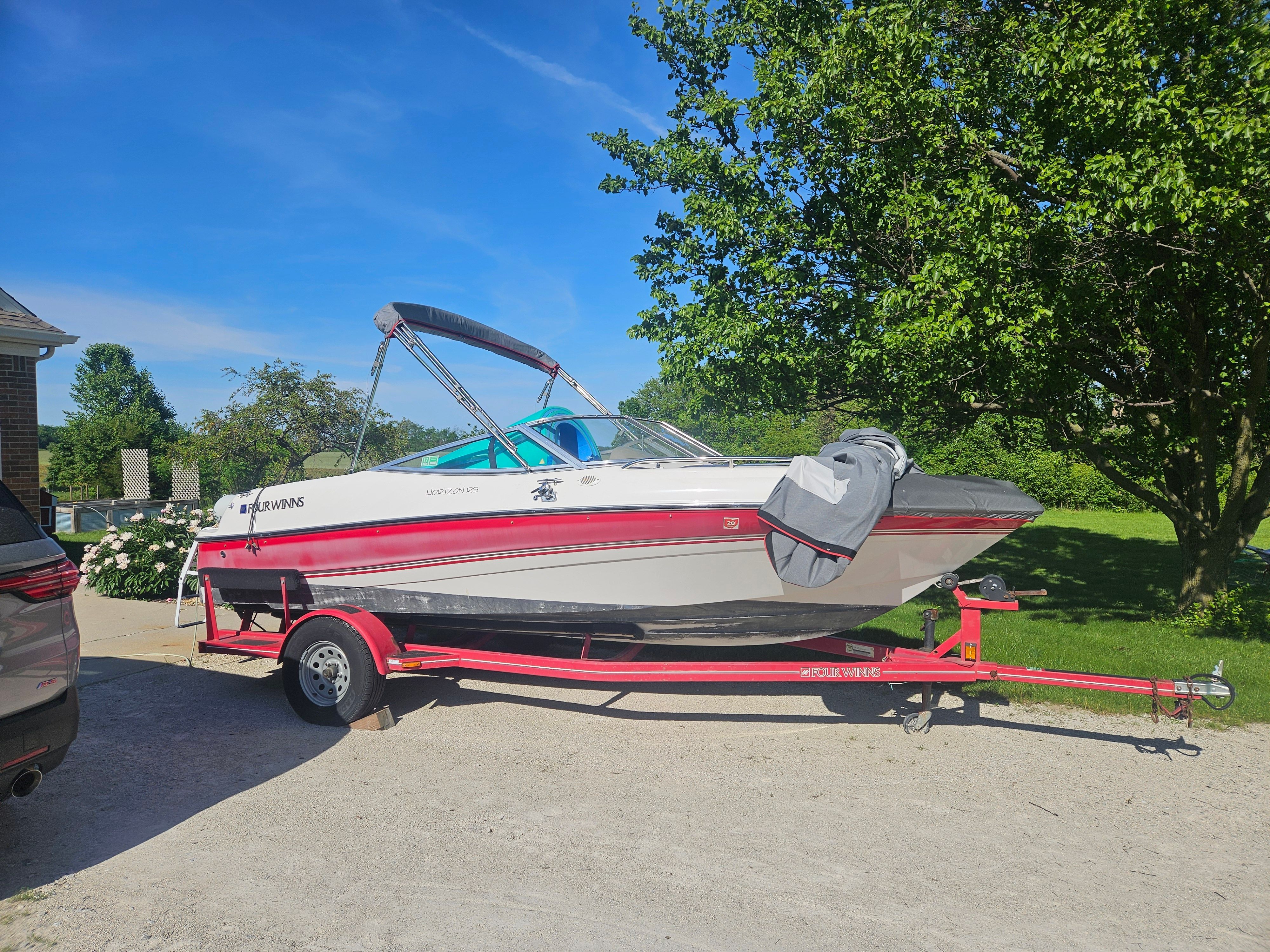 A 1997 Four Winns Horizon boat on a red trailer, parked on a driveway next to a tree.