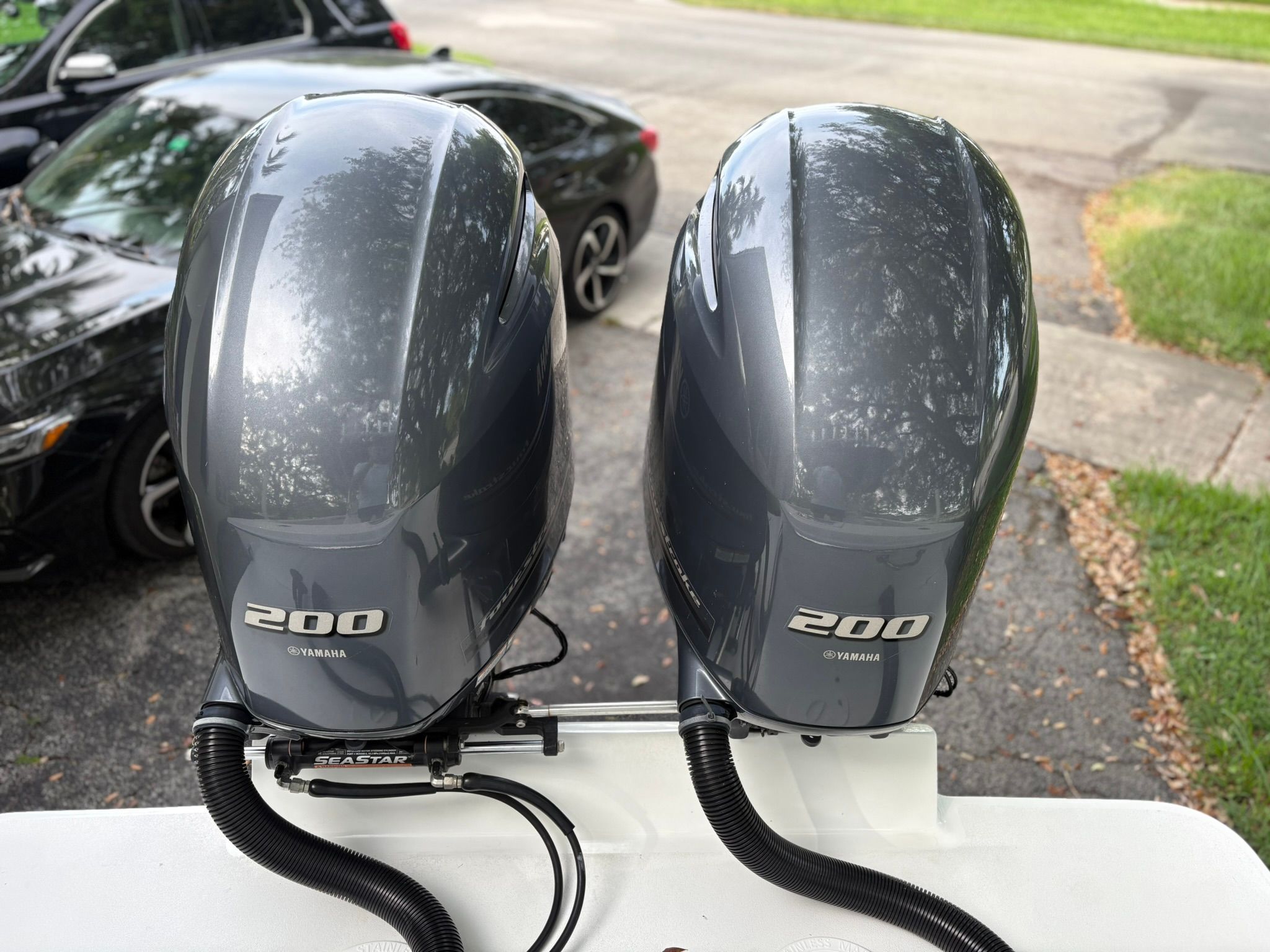Two Yamaha 200 outboard motors are mounted on a boat parked in a driveway.