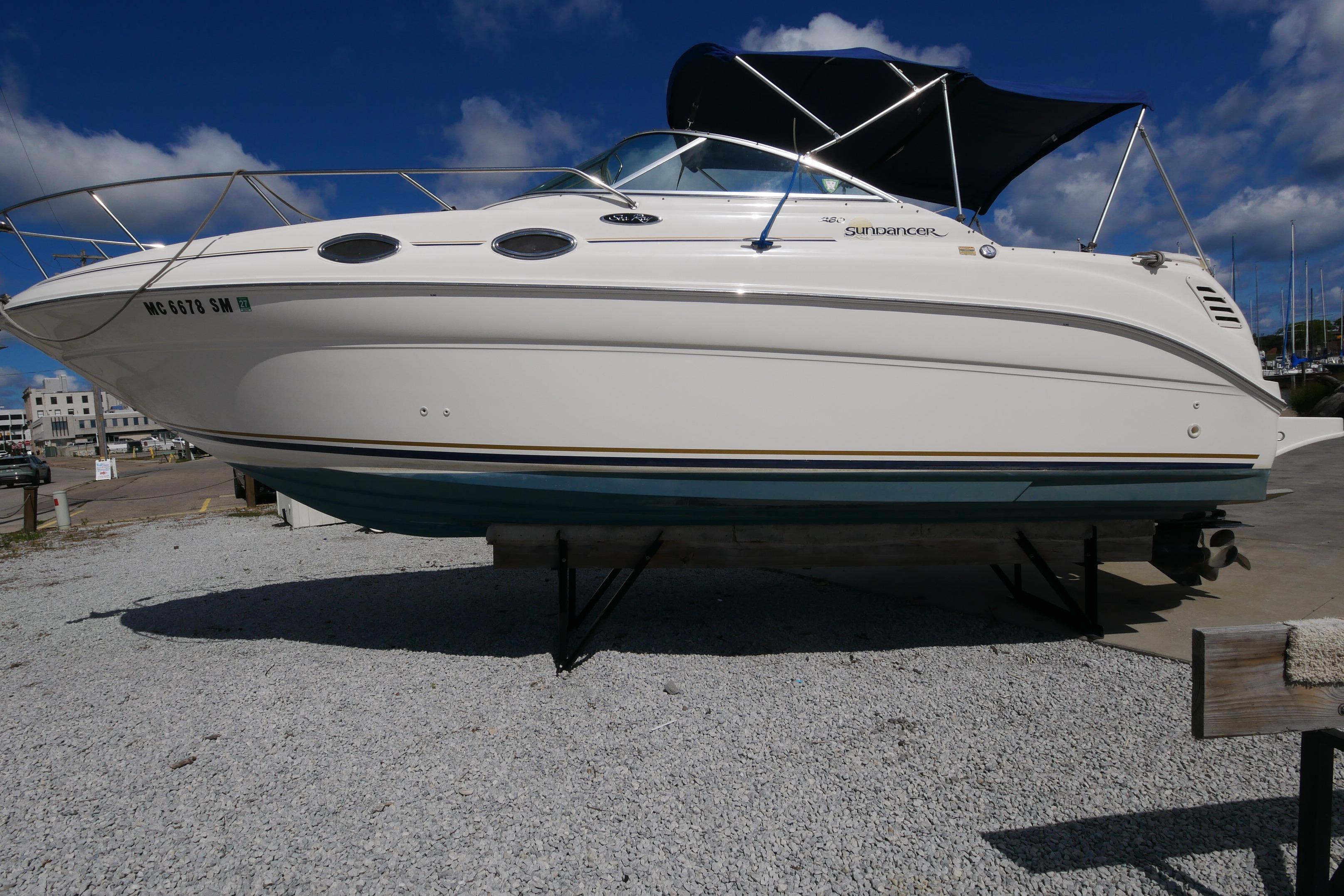 2003 Sea Ray 260 Sundancer boat on dry dock, white hull, blue canopy, sunny day.