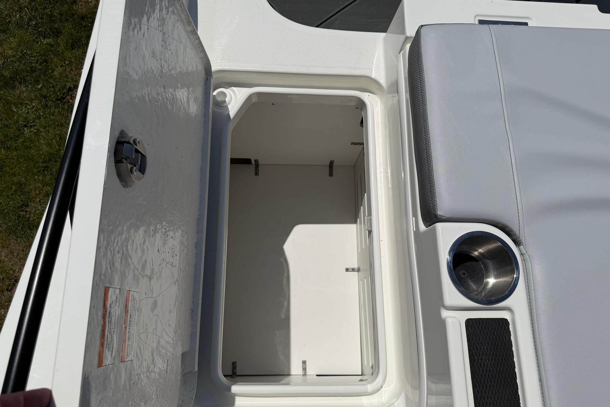 Open storage compartment on 2026 Bayliner D20 boat with cup holder and cushioned seating.