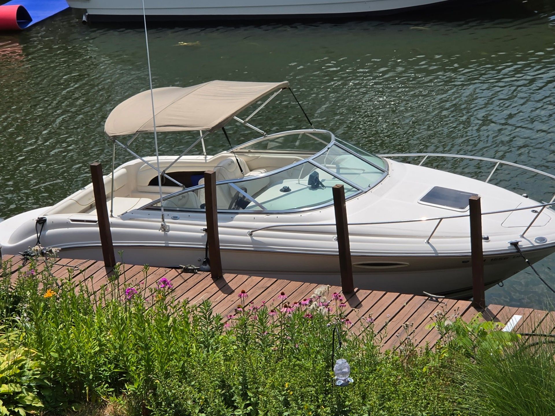 A 2002 Sea Ray 225 Weekender docked at a wooden pier. It features a beige canopy.
