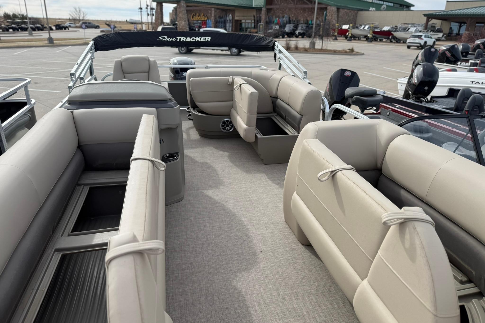 2025 Sun Tracker Party Barge 18 DLX interior with beige seating in a parking lot.