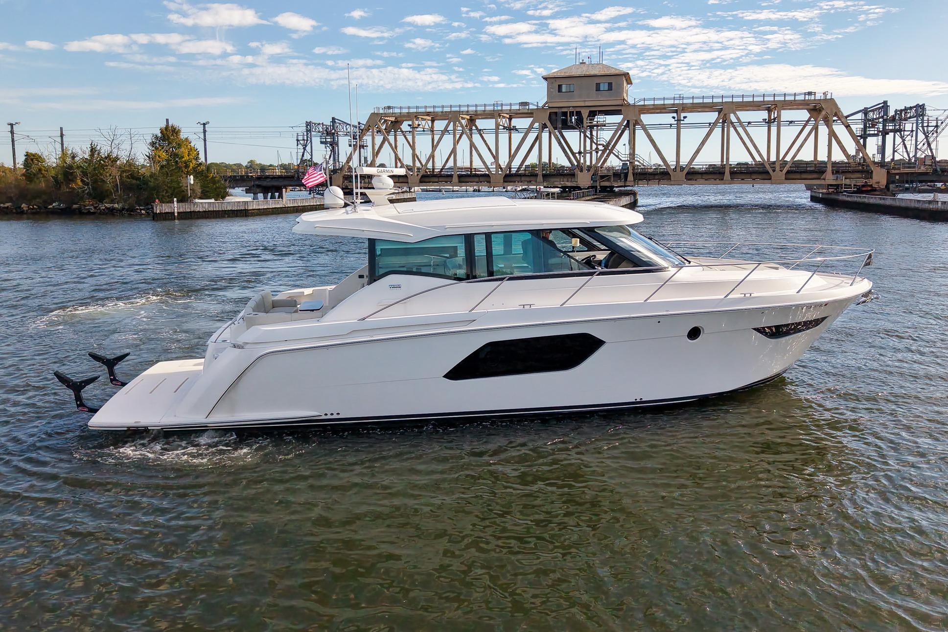 2019 Tiara Yachts C49 Coupe cruising on a river with a bridge in the background.