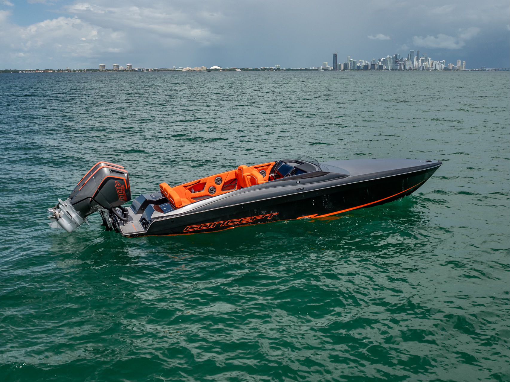 A modern sport boat with orange seats on the water, with a city skyline in the background.