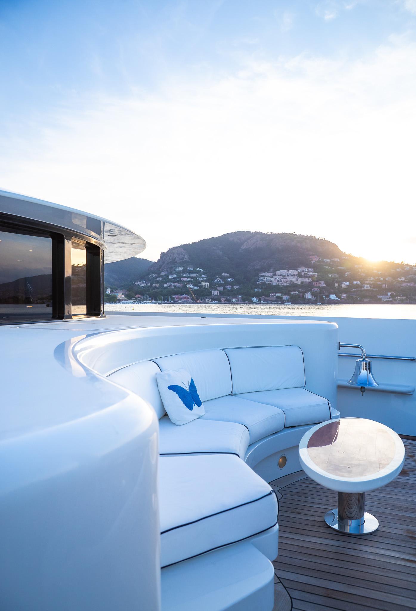 Luxurious Benetti 60 yacht deck with elegant seating, scenic ocean view, and sunset backdrop.