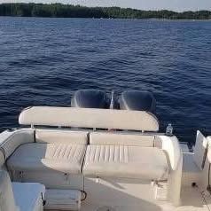 The image shows the stern of a boat with seating and two outboard motors on a calm lake.