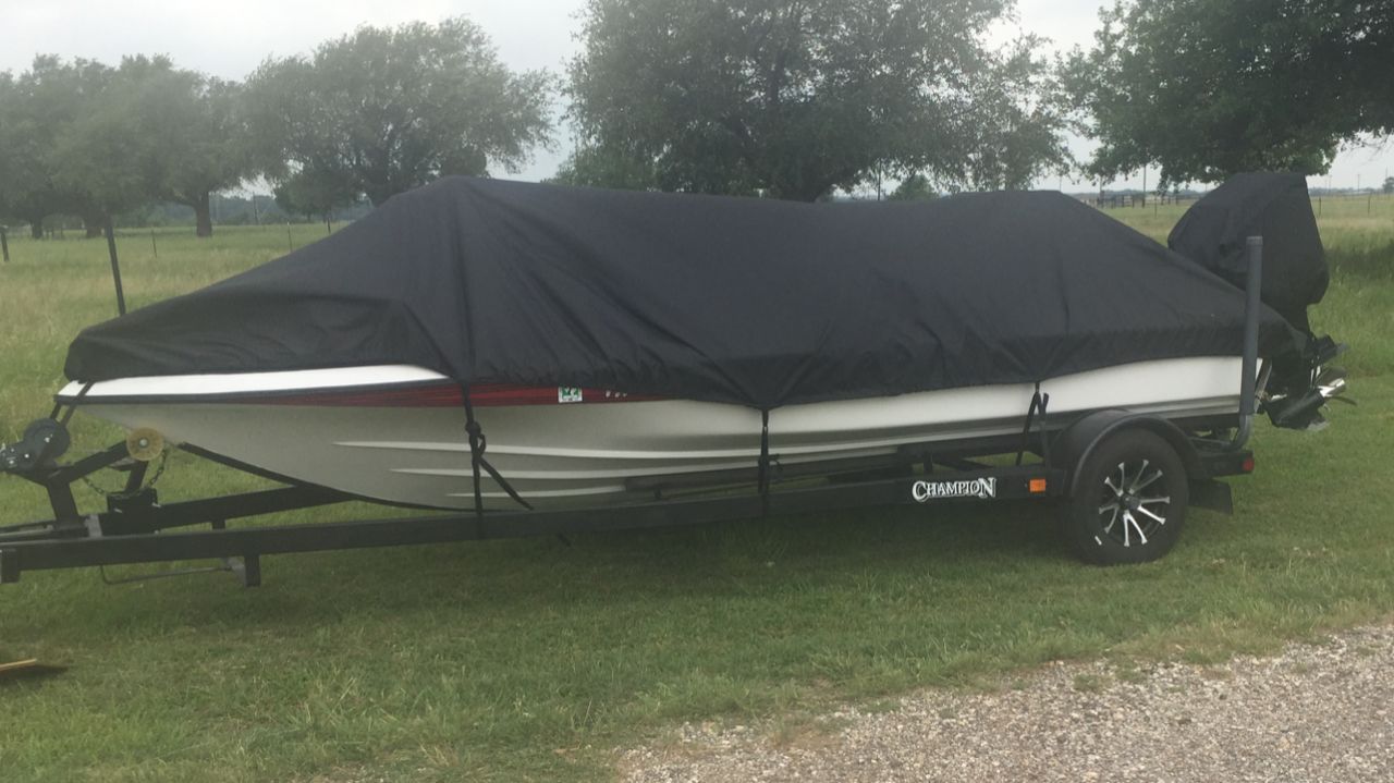 A 1999 Champion Bass boat with a black cover on a trailer, parked on a grassy area.