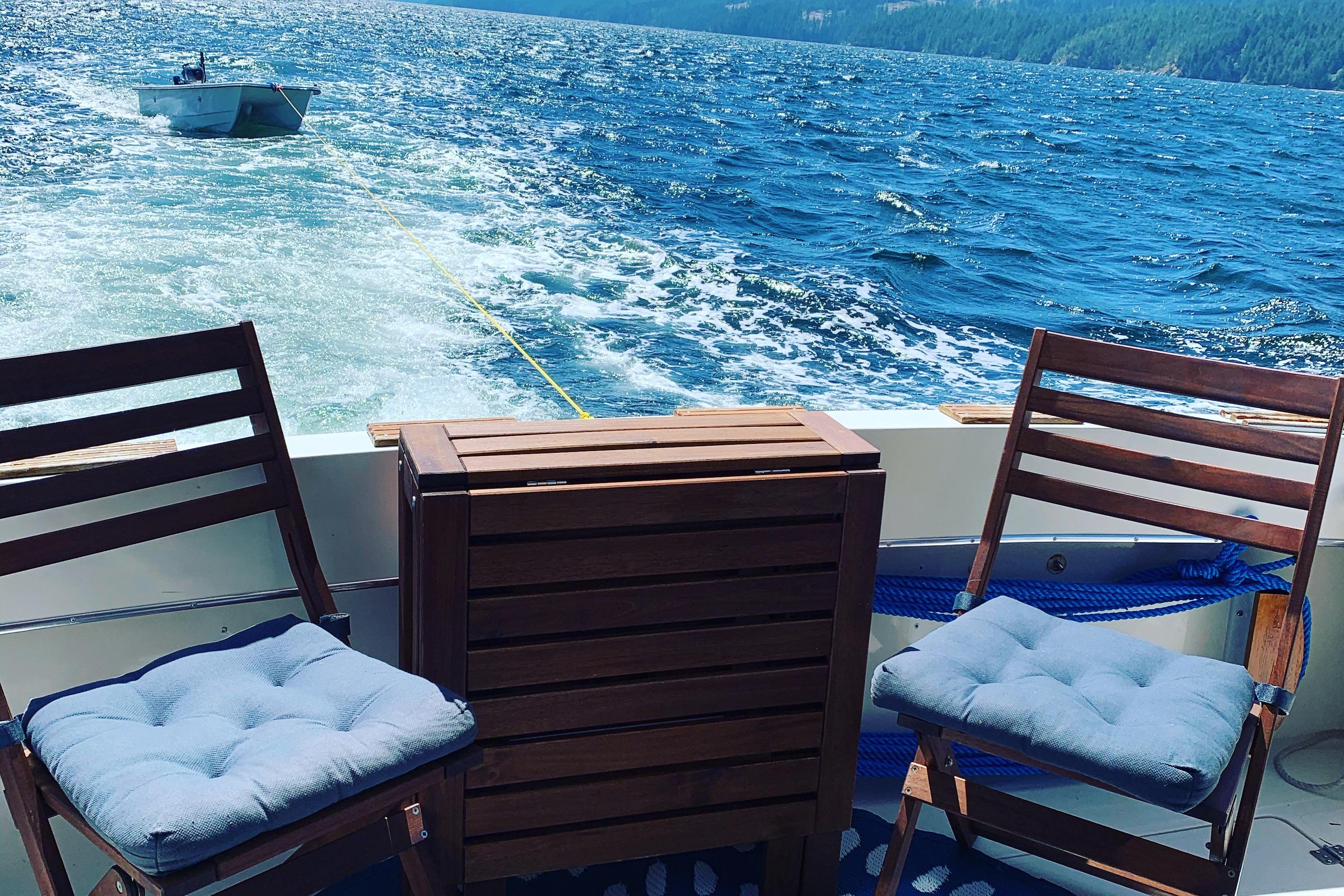 1984 Bayliner 3270 Explorer with chairs and table on deck, towing a small boat.