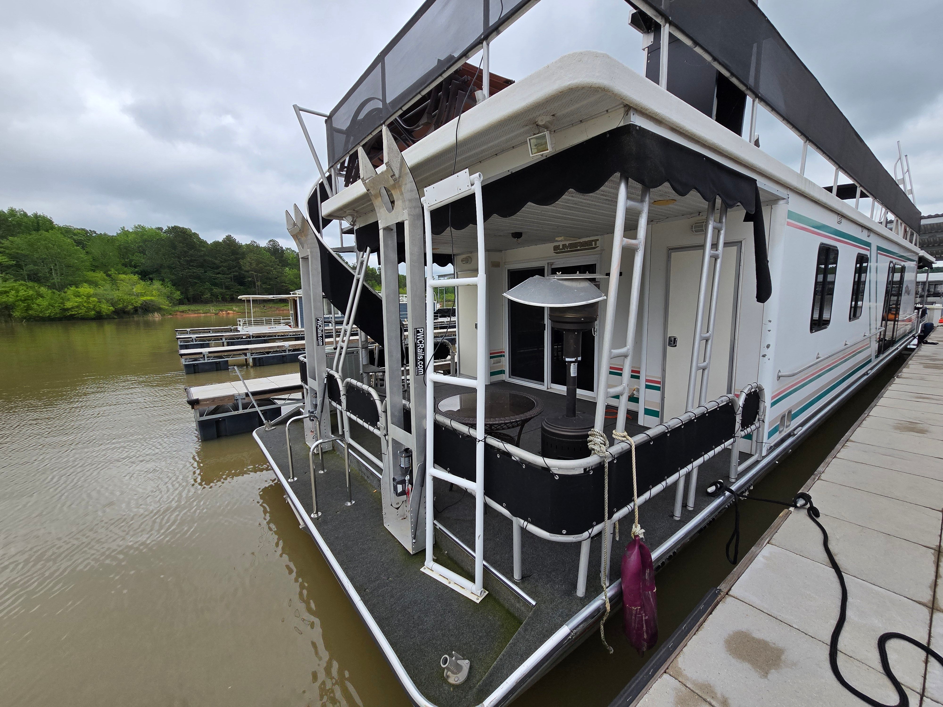 1998 Sumerset houseboat docked on a calm lake with lush green surroundings.