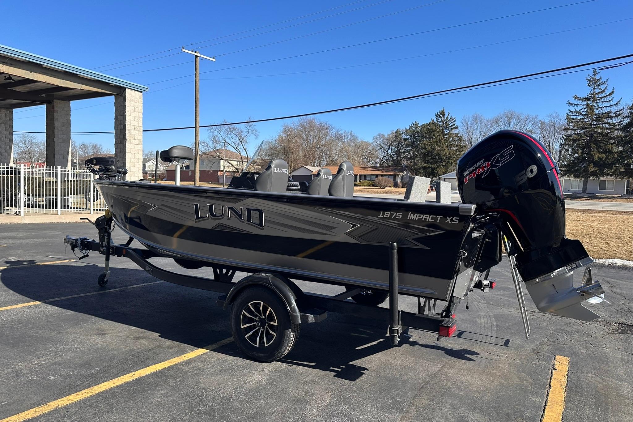 2026 Lund 1875 Impact XS SS boat with Mercury engine, parked outdoors on a sunny day.