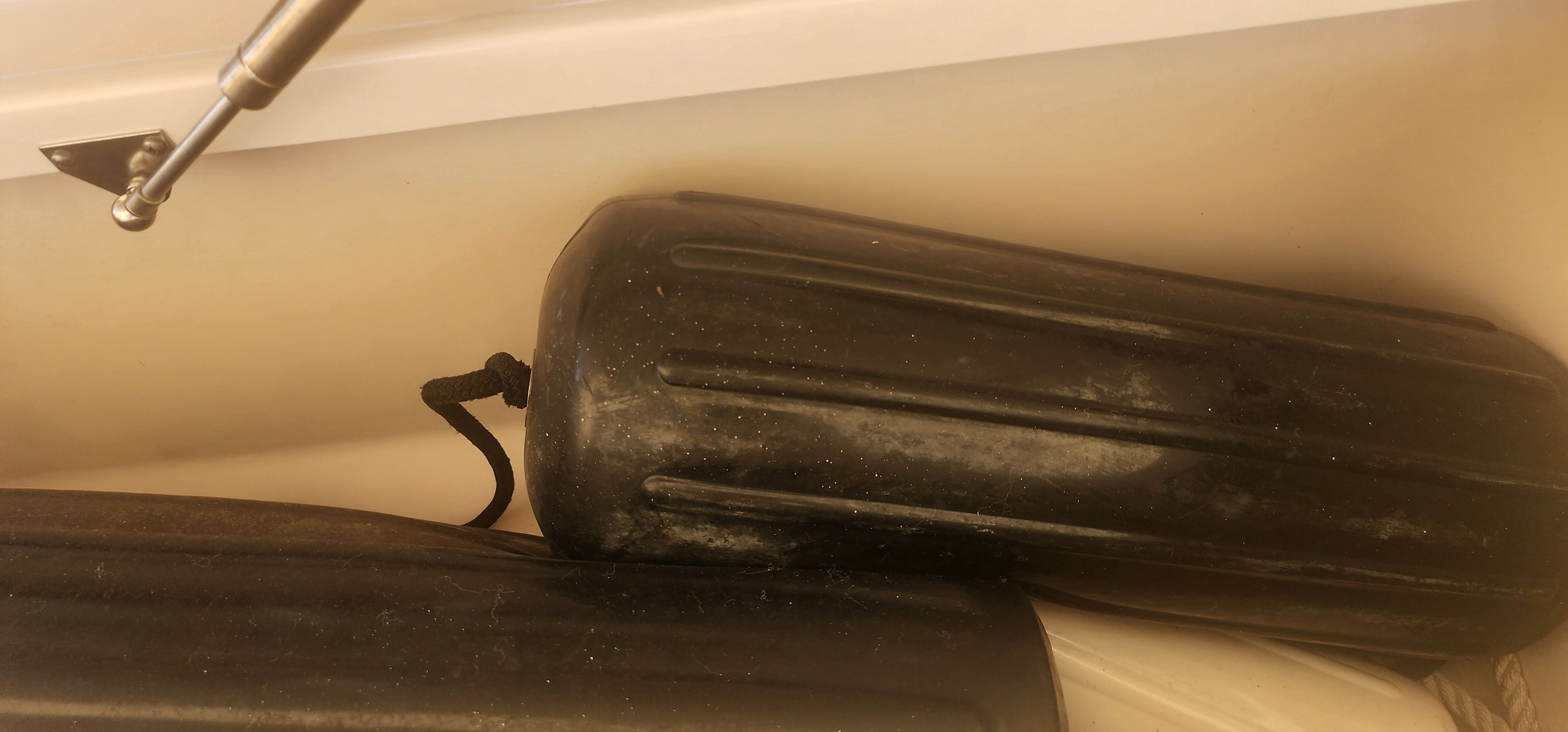 Two black boat fenders are stored in a compartment. A metal arm is visible.