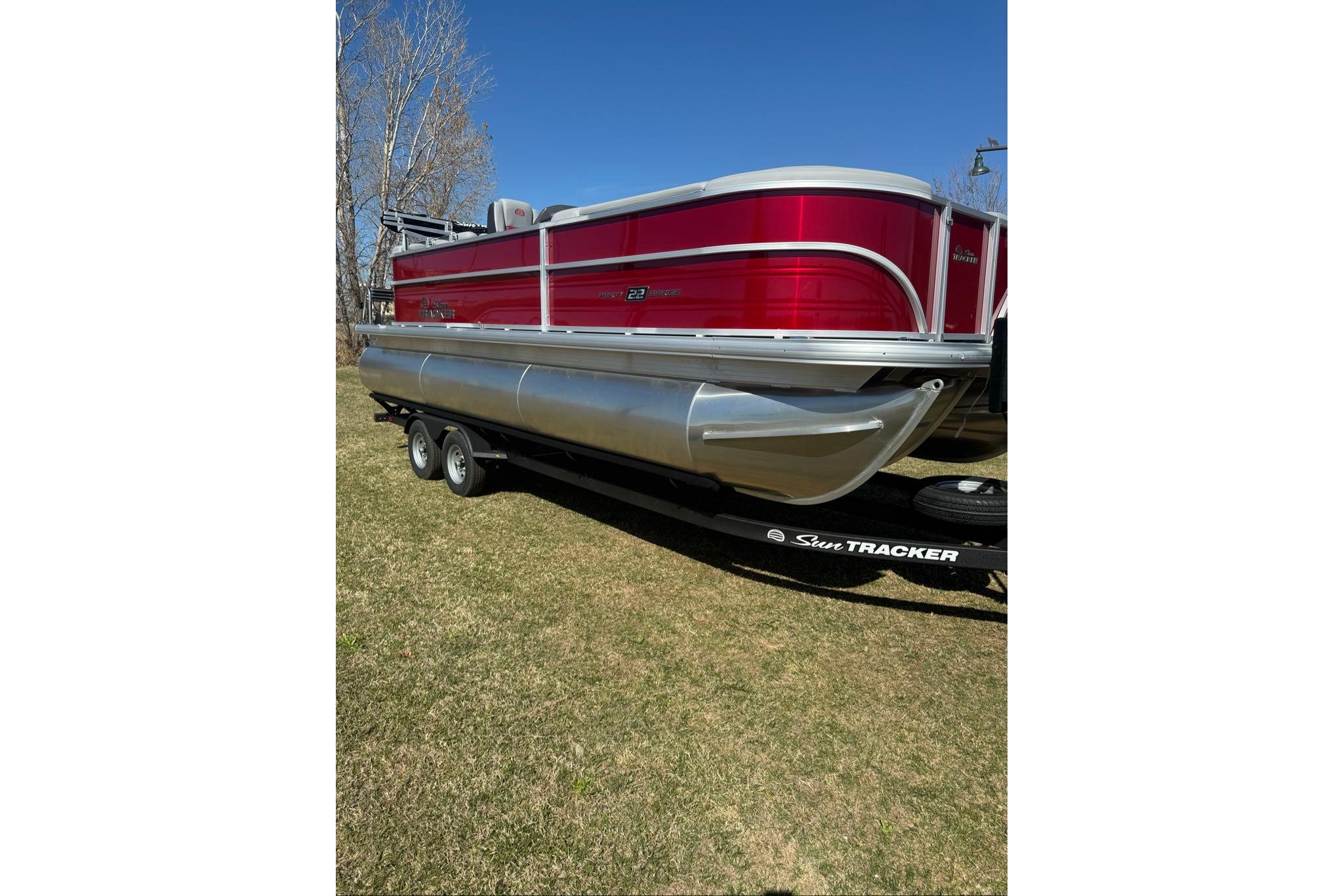 2026 Sun Tracker Party Barge 22 XP3 pontoon boat on trailer, parked on grass.