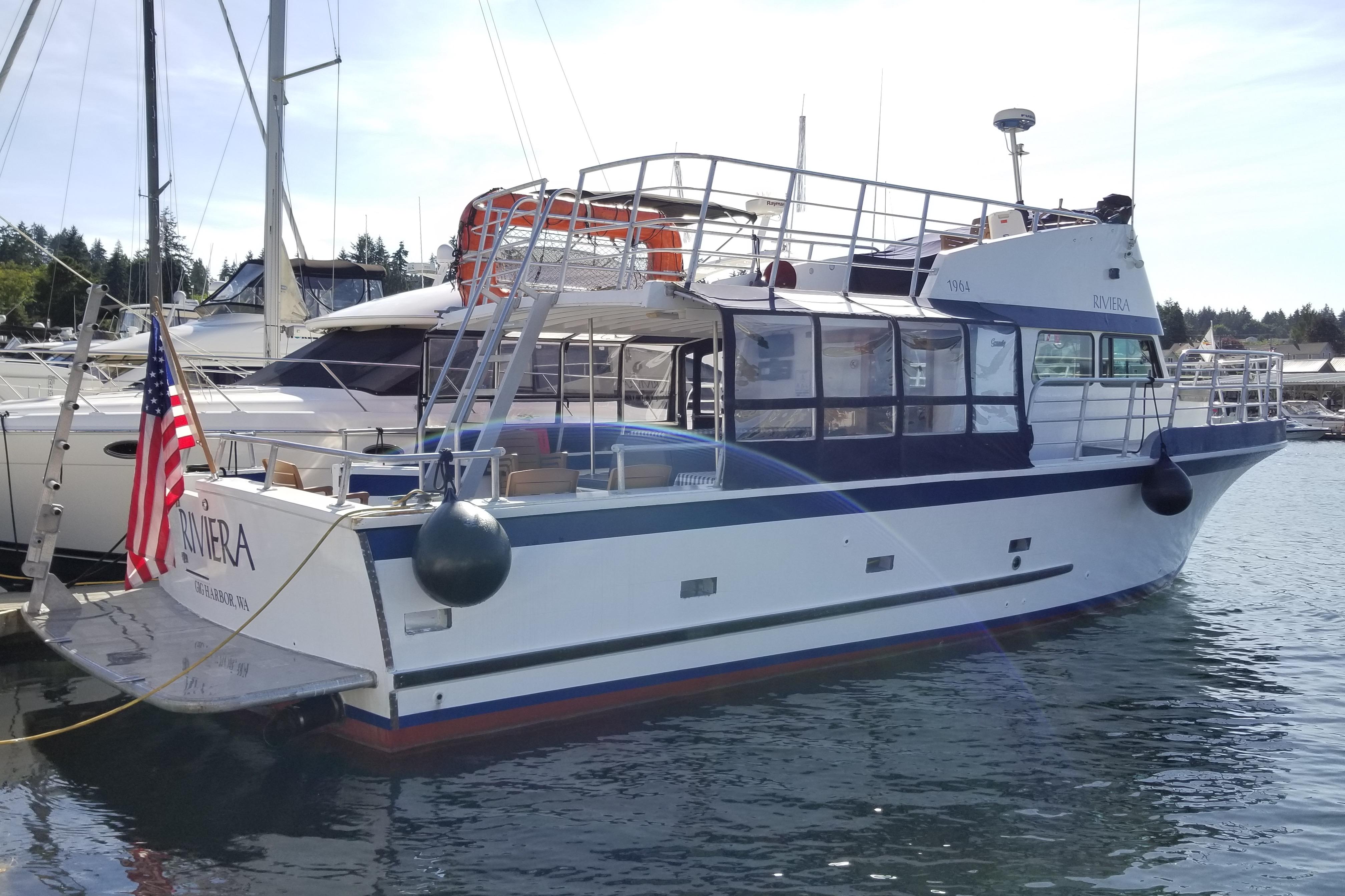 1964 Grandy Tour Boat docked, featuring American flag and marina backdrop.
