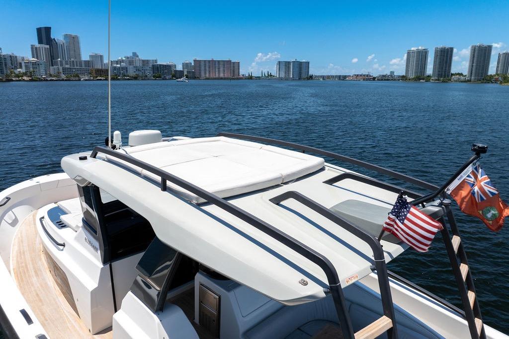 Bluegame BG 42 yacht cruising near city skyline, 2021 model, with flags displayed.