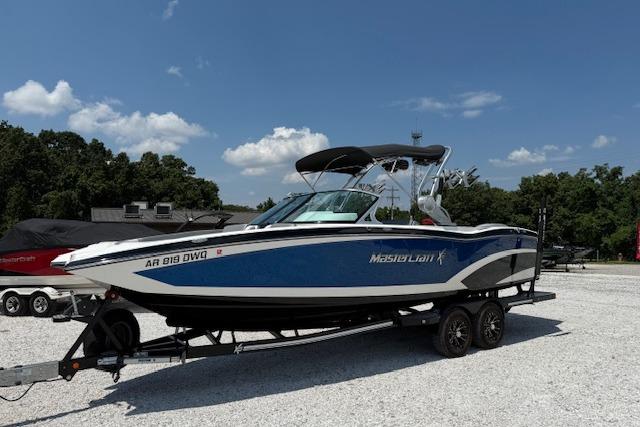 2016 MasterCraft X26 boat on trailer, blue and white, parked outdoors.