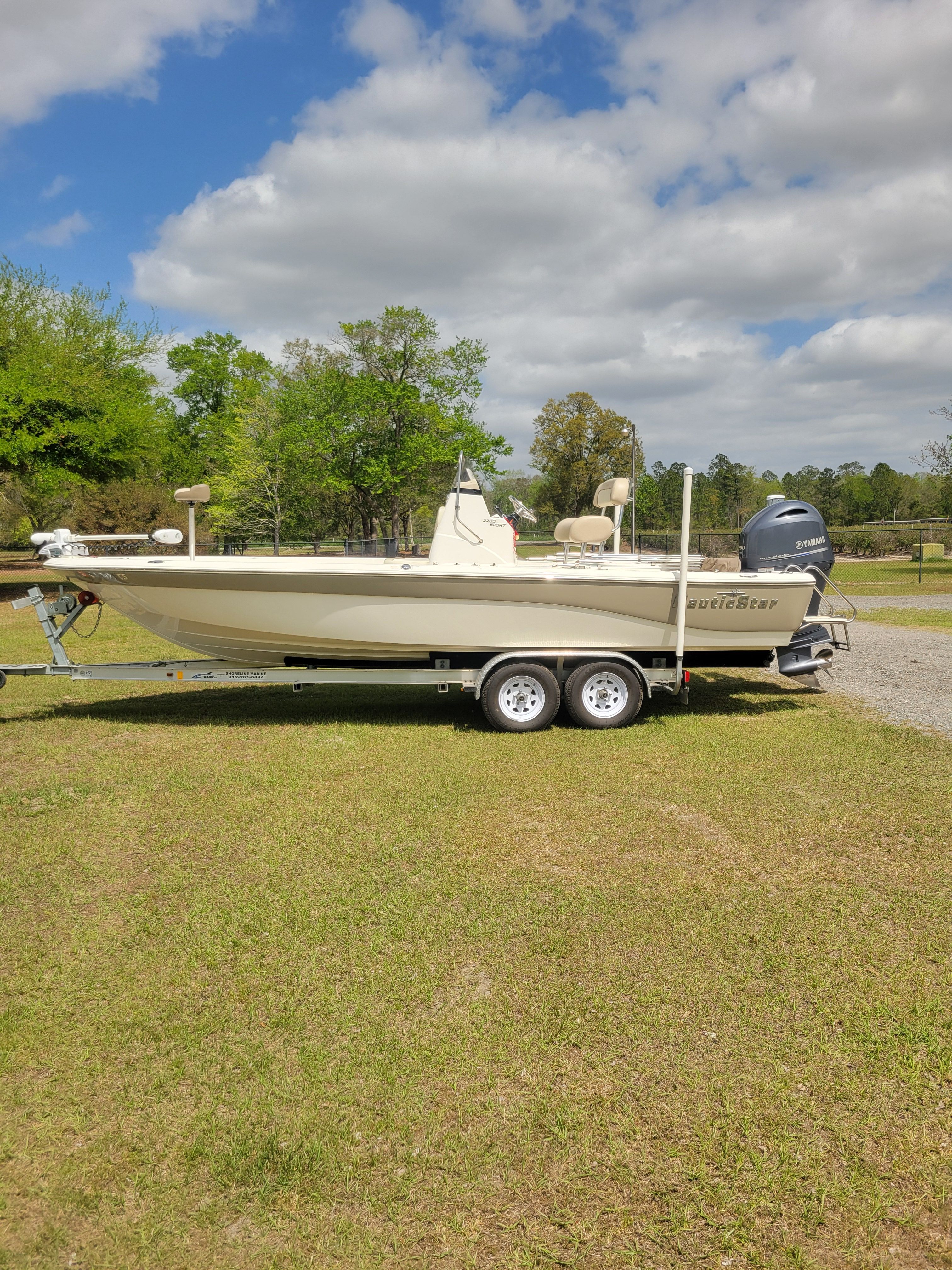 A NauticStar 2200 Sport boat on a trailer, surrounded by trees and grass.