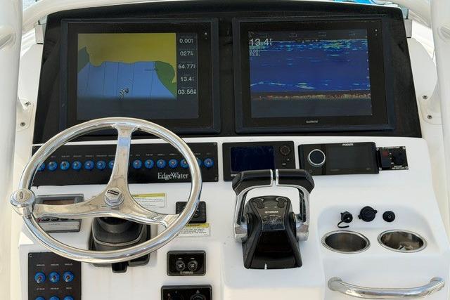 Control panel of a 2014 Edgewater 318CC boat with navigation screens and steering wheel.