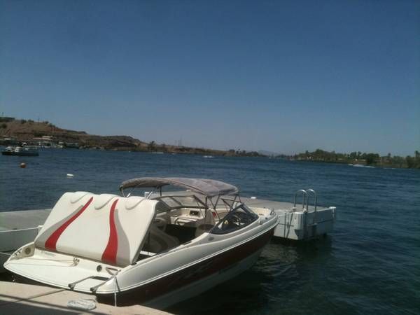 A white boat with a red stripe is docked on calm water.