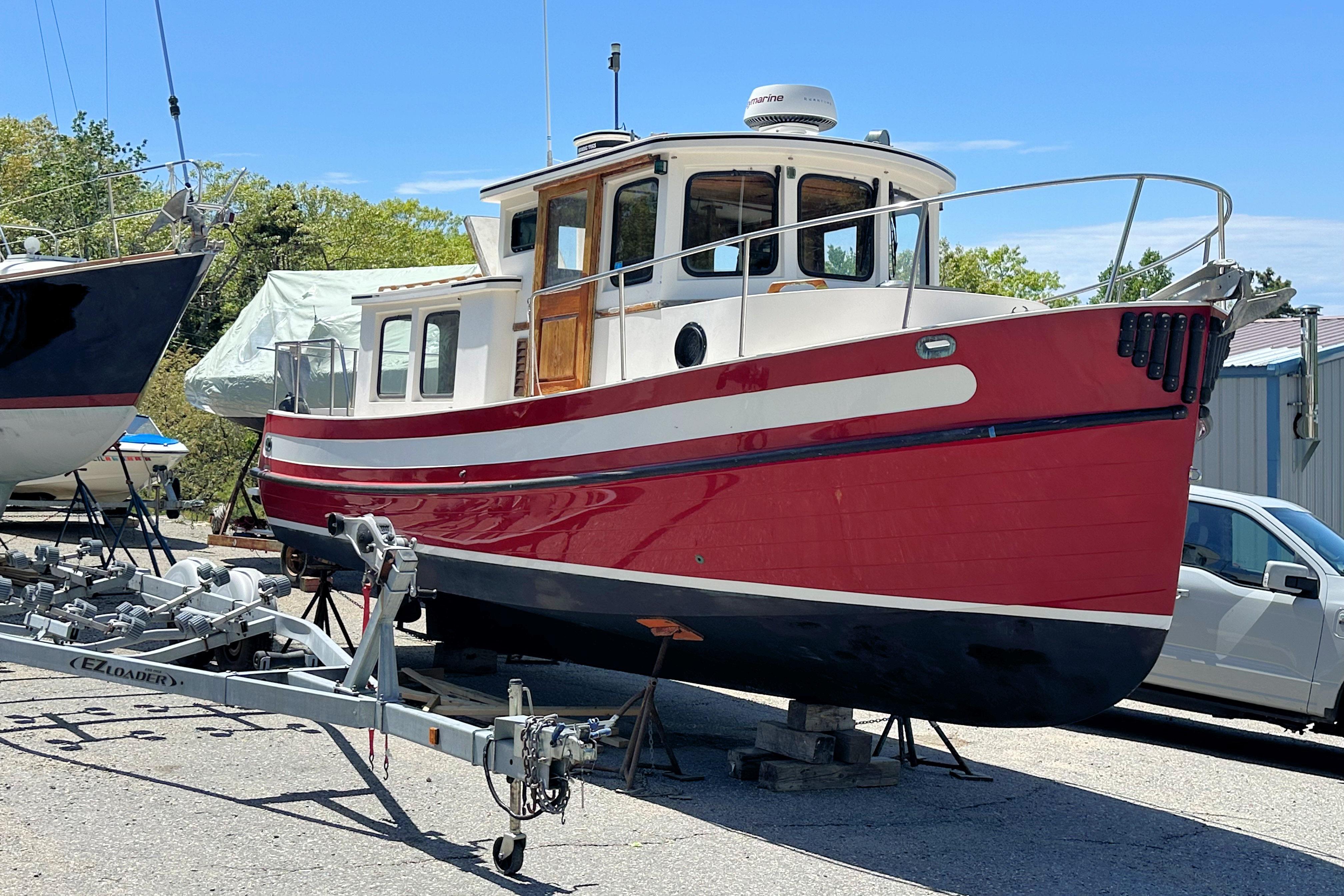 1985 Nordic Tug 26 boat on trailer, red and white, parked outdoors.