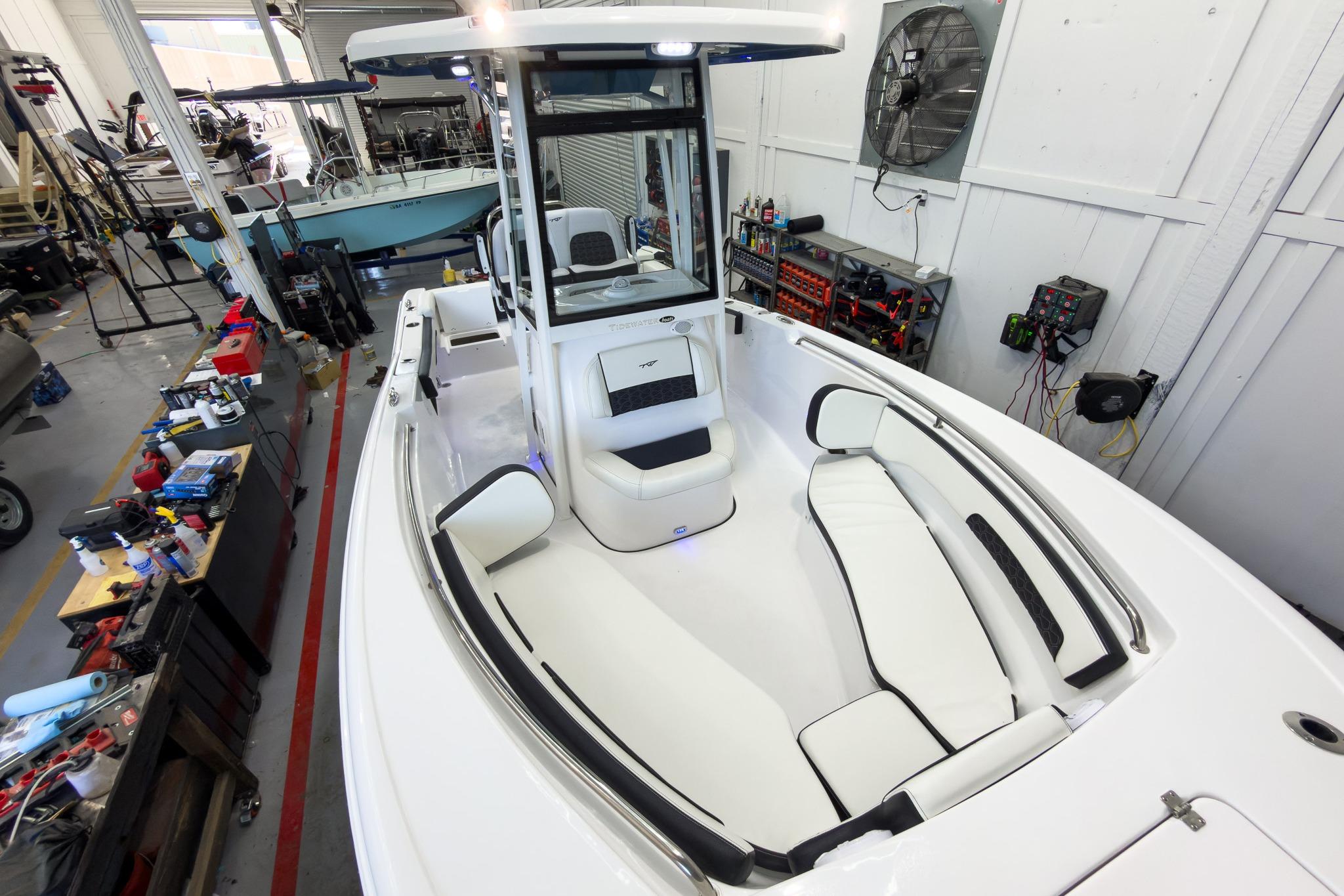 The image shows a modern boat with white upholstery and a helm station. It's in a workshop.