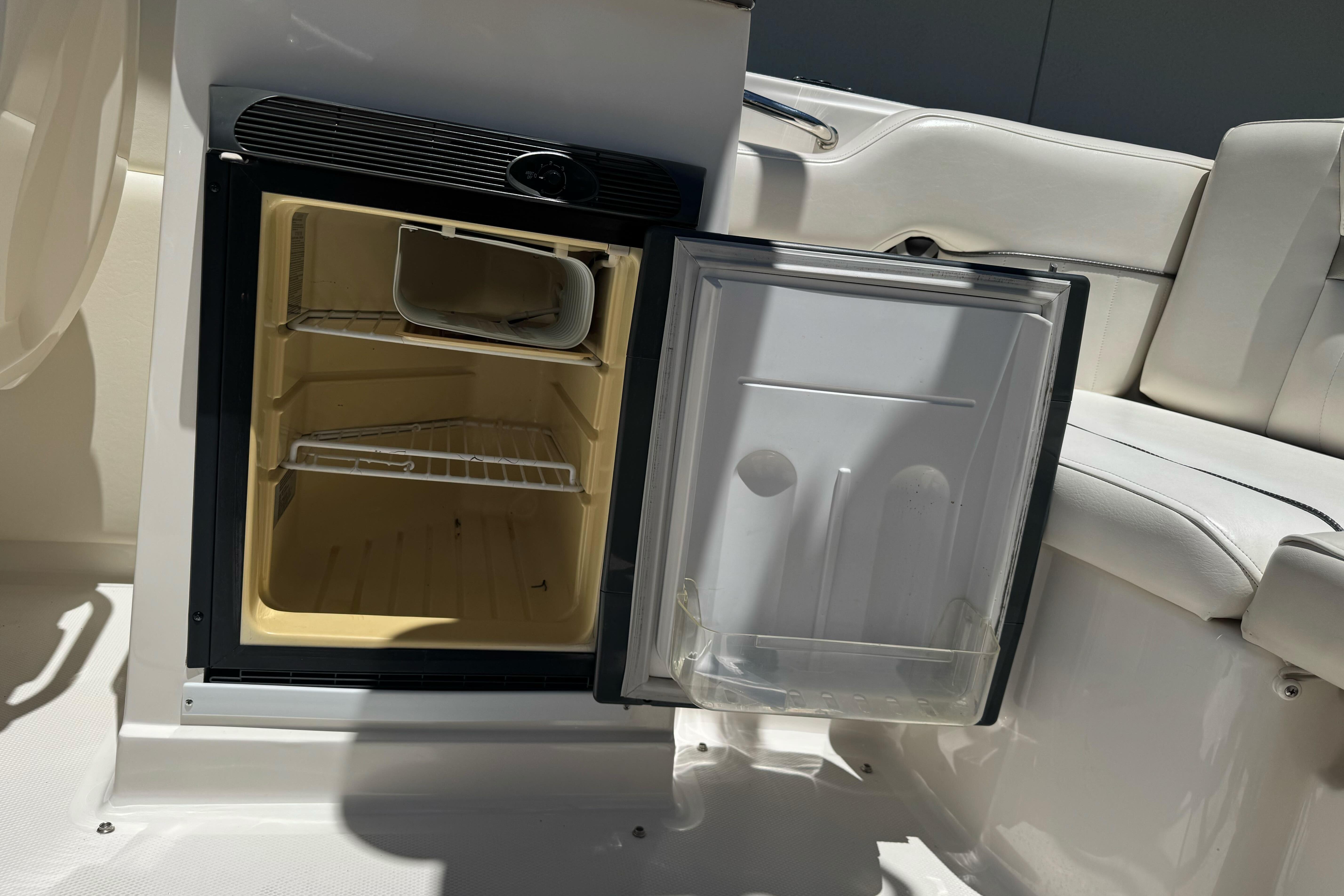Open mini fridge on 2007 Sea Ray SLX 250 boat, showcasing interior shelves and seating area.