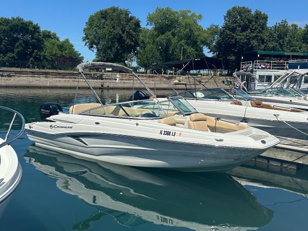 2023 Crownline 215 XS boat docked in a marina, surrounded by trees and other boats.