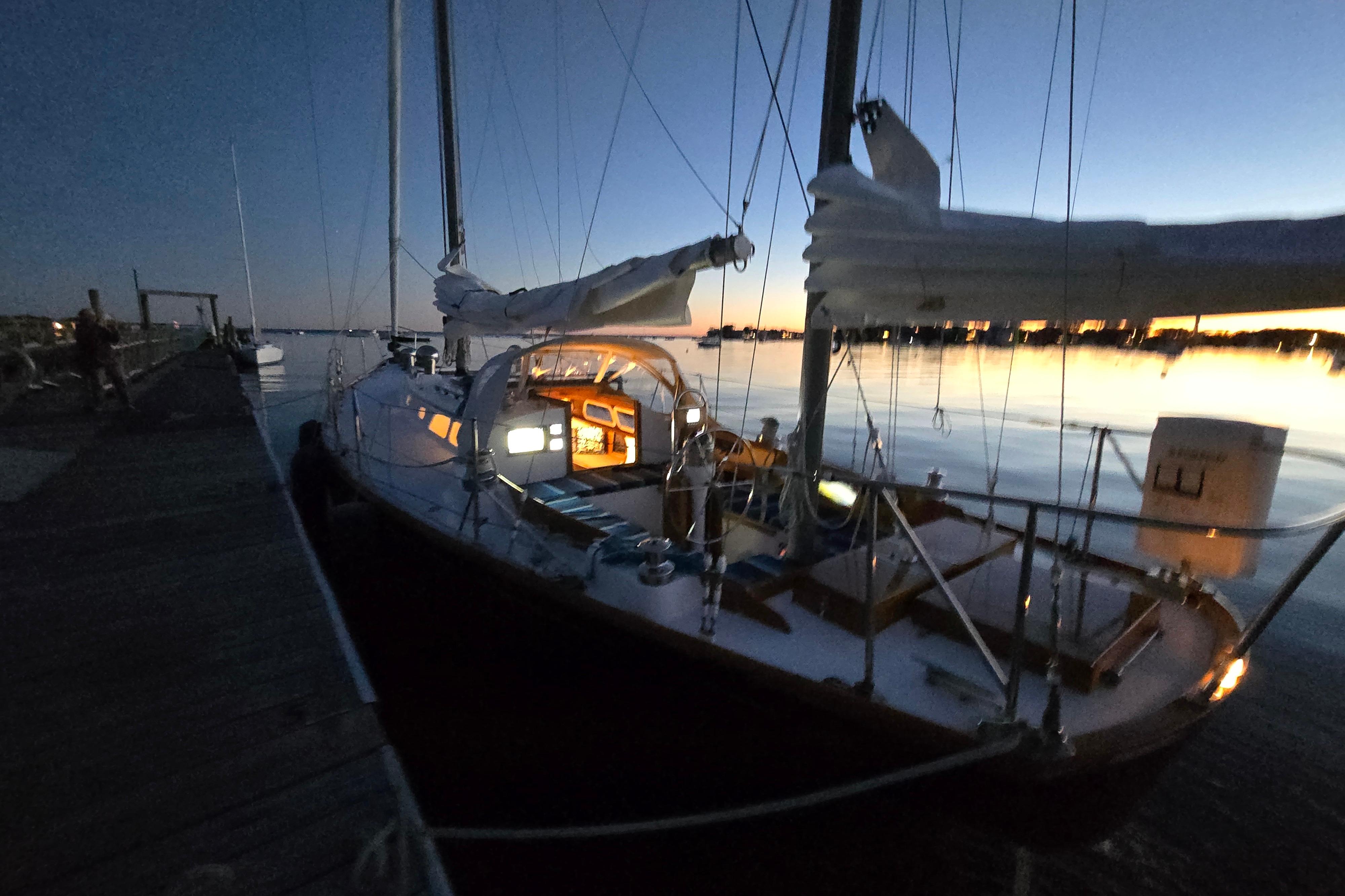 1970 Hinckley Bermuda 40 sailboat docked at sunset with illuminated cabin interior.