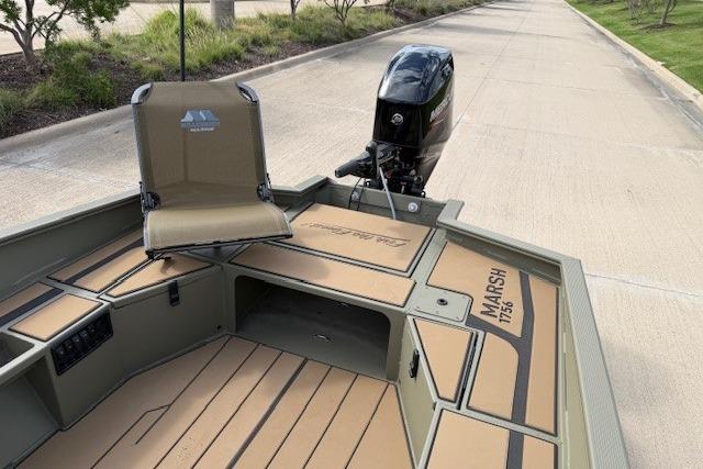 2026 Tracker Grizzly 1756 T Marsh boat with seating and motor on a paved road.