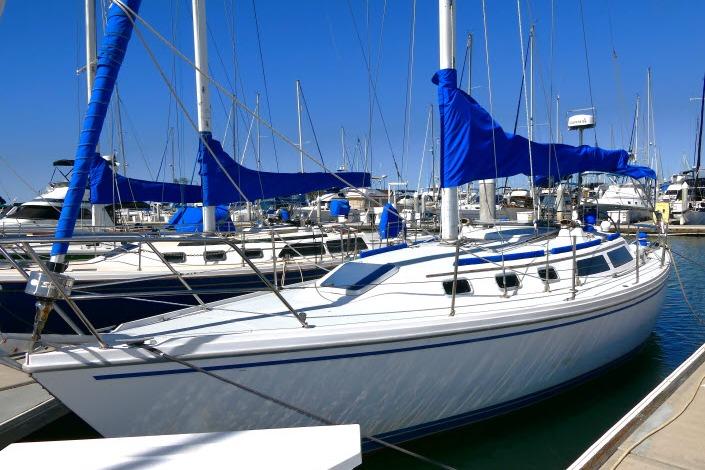 1989 Catalina 34 sailboat docked in marina, featuring blue sails and clear sky.