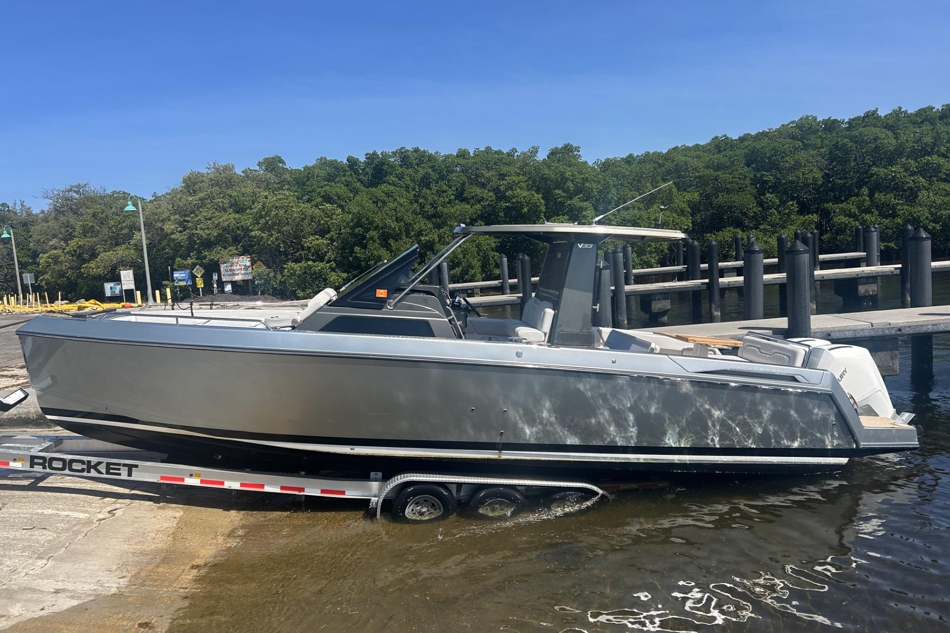 2023 Schaefer V33 boat on trailer at dockside, surrounded by lush greenery.